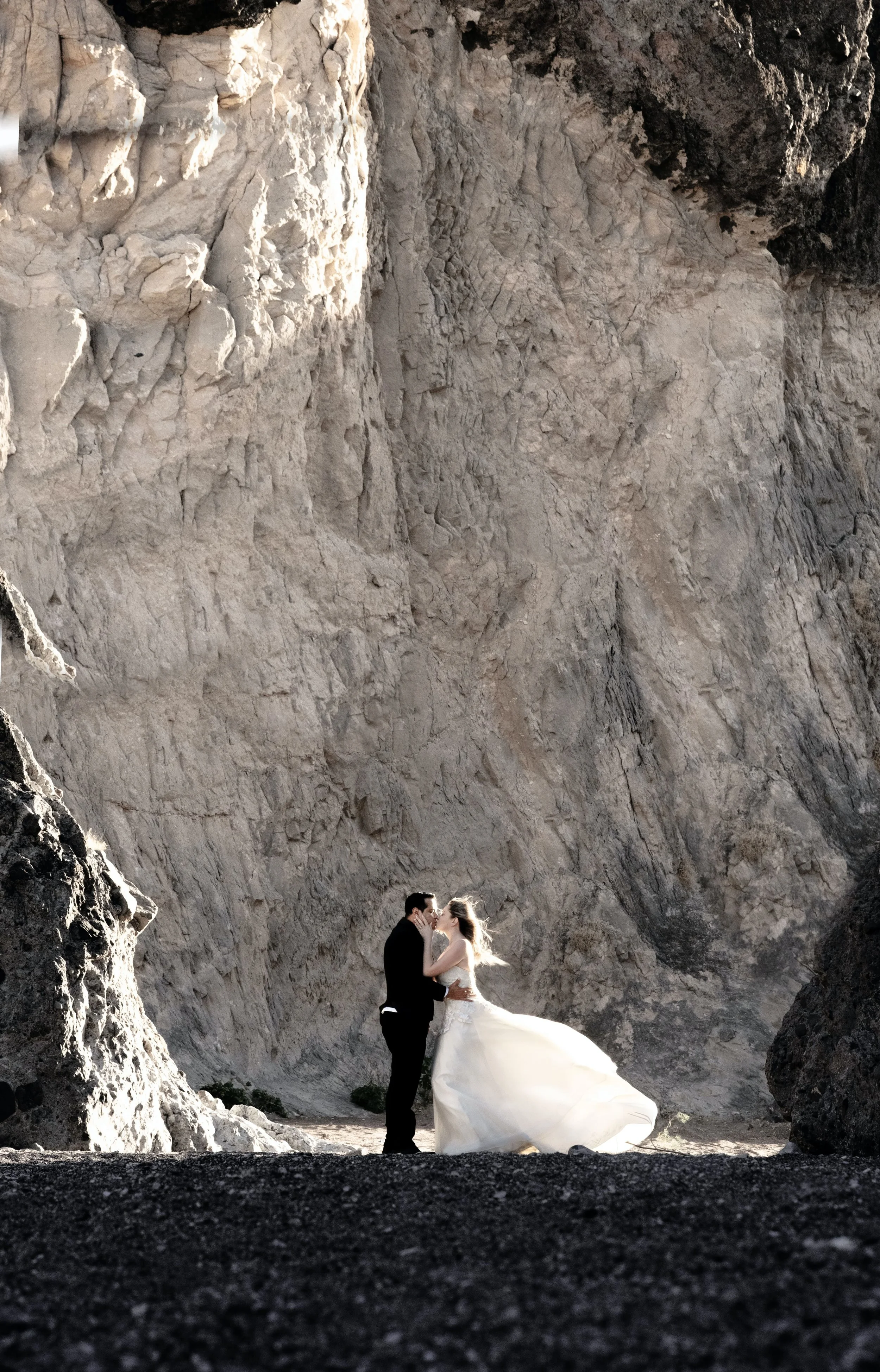 A bride and groom in wedding attire standing and touching foreheads in a rocky, canyon-like setting with towering walls of rock around them.