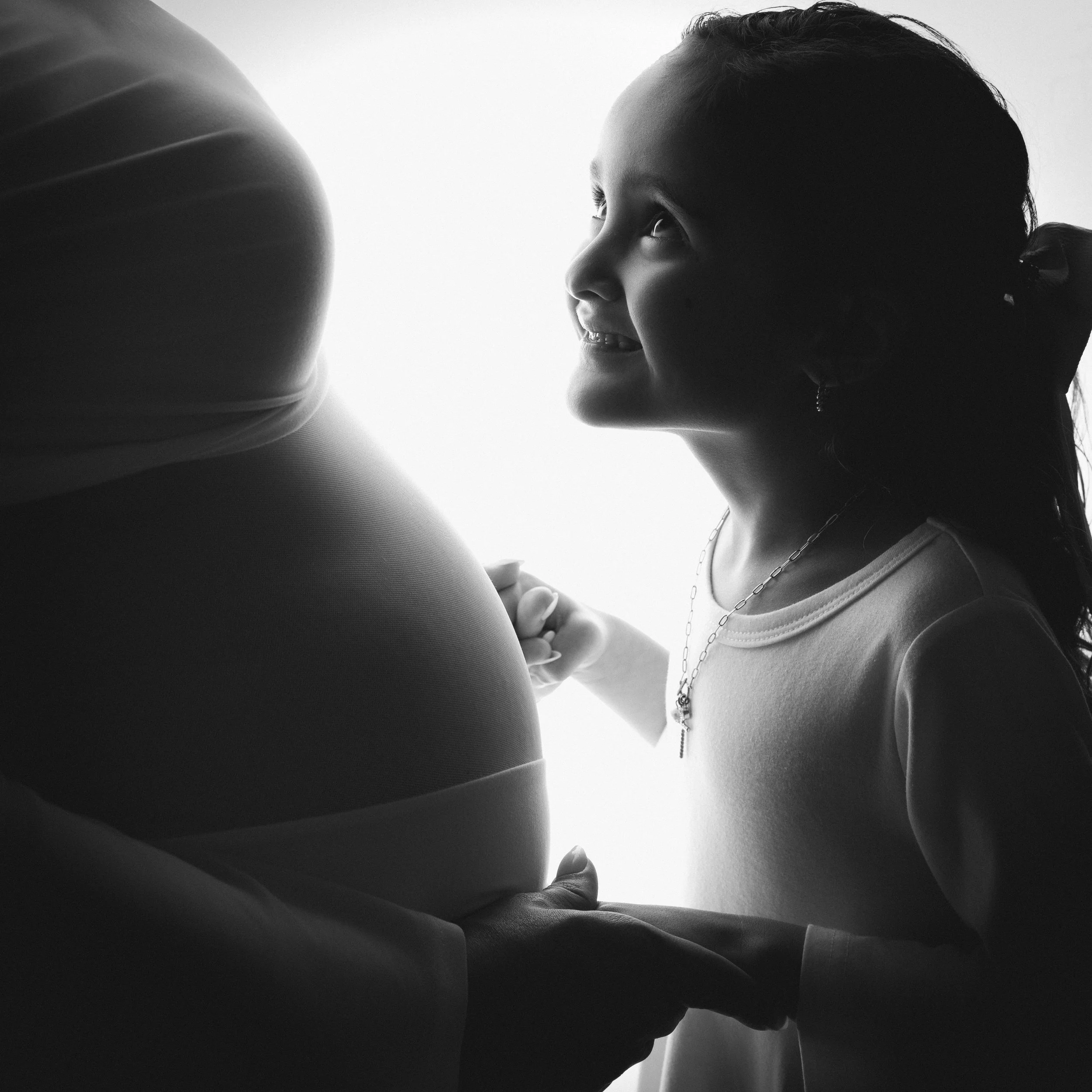 Daughter holding her mother’s hands and smiling at her baby bump during a Southern California maternity photography session serving the Inland Empire, Orange County, and Los Angeles County.