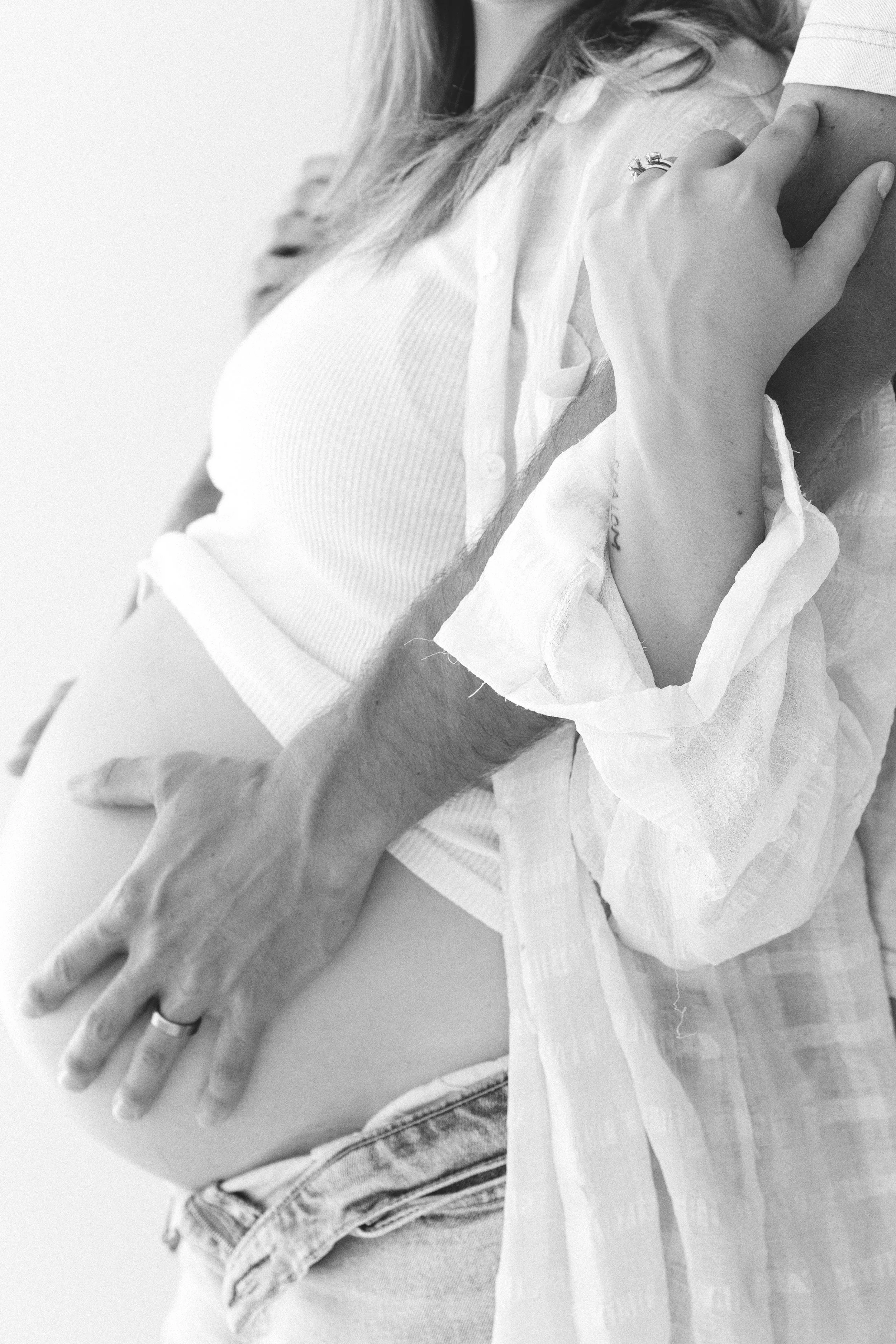 A woman wearing a white shirt, with her hand resting on top of an arm, wearing a ring on her finger.
