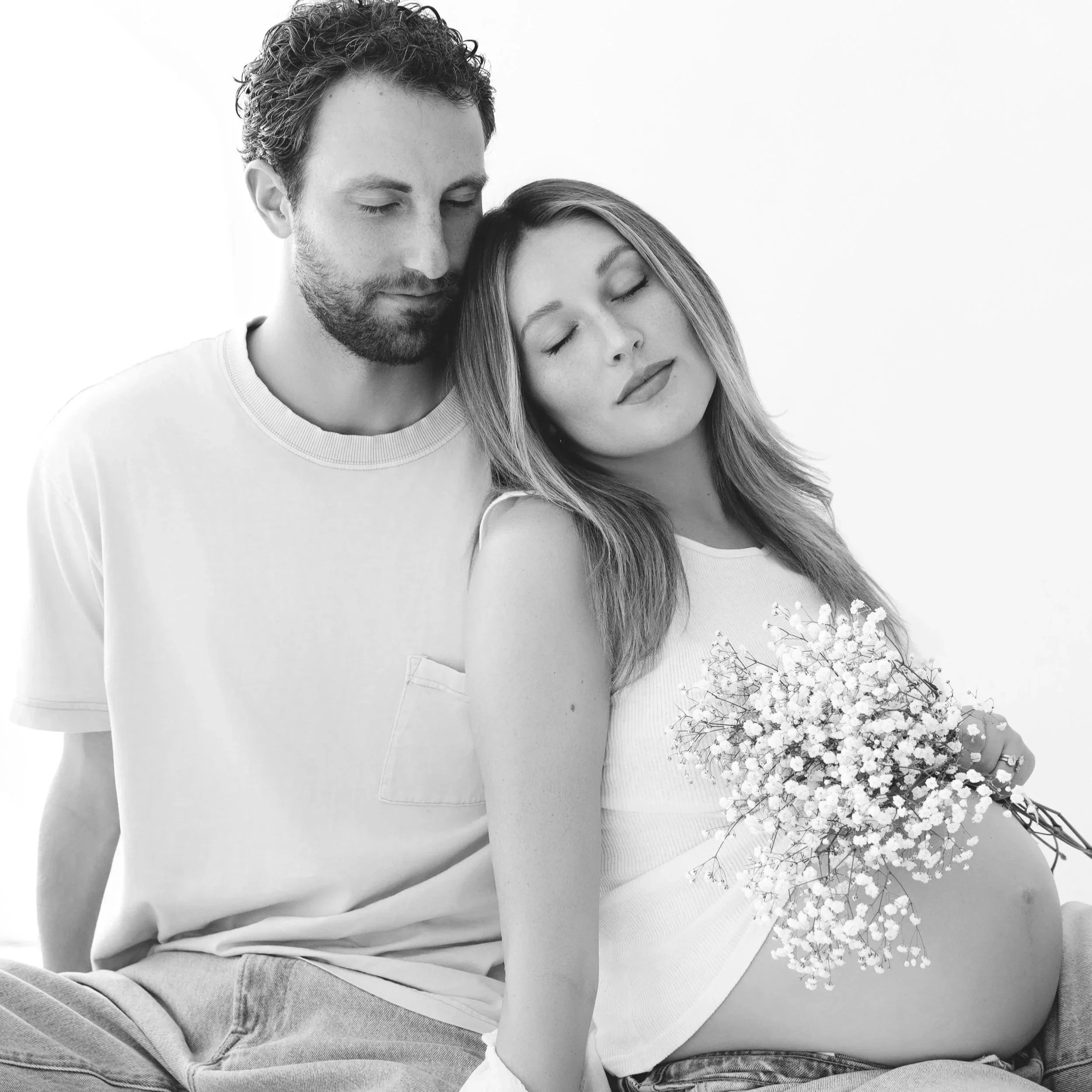 A black-and-white photo of a man and a woman with closed eyes, close to each other, with the woman holding a bouquet of small white flowers.