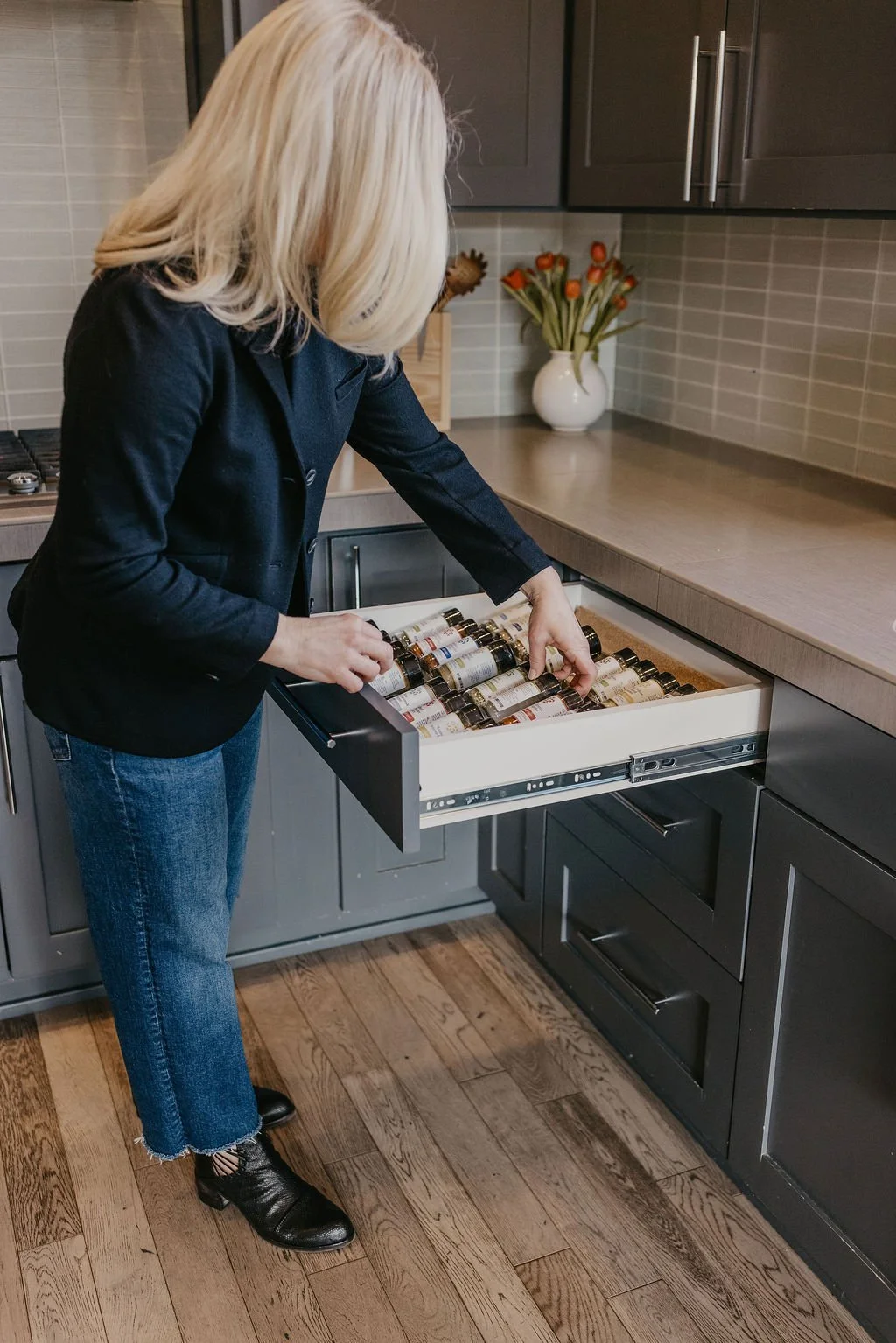 Woman organizing medication bottles in a kitchen drawer.