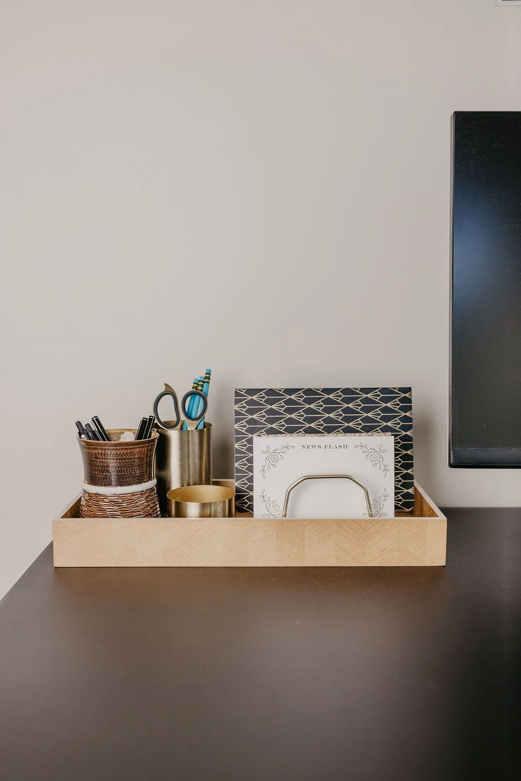 Desk organizer containing pens, scissors, notebooks, and a folder on a black desk against a plain white wall.