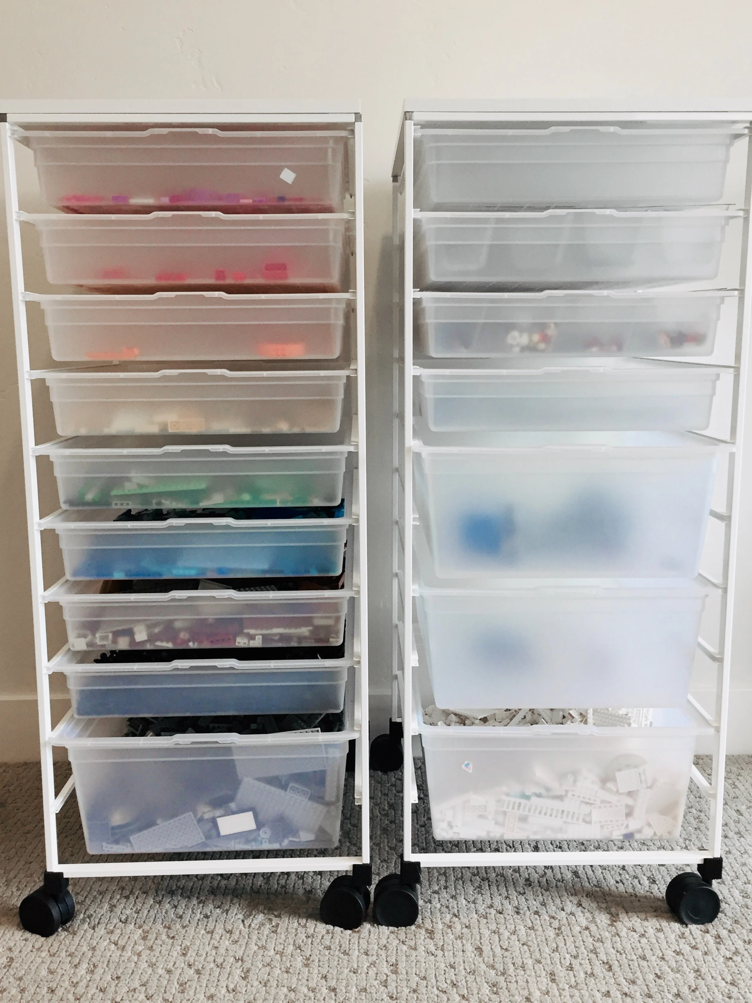 Two white storage carts with multiple plastic drawers filled with LEGO bricks and pieces.