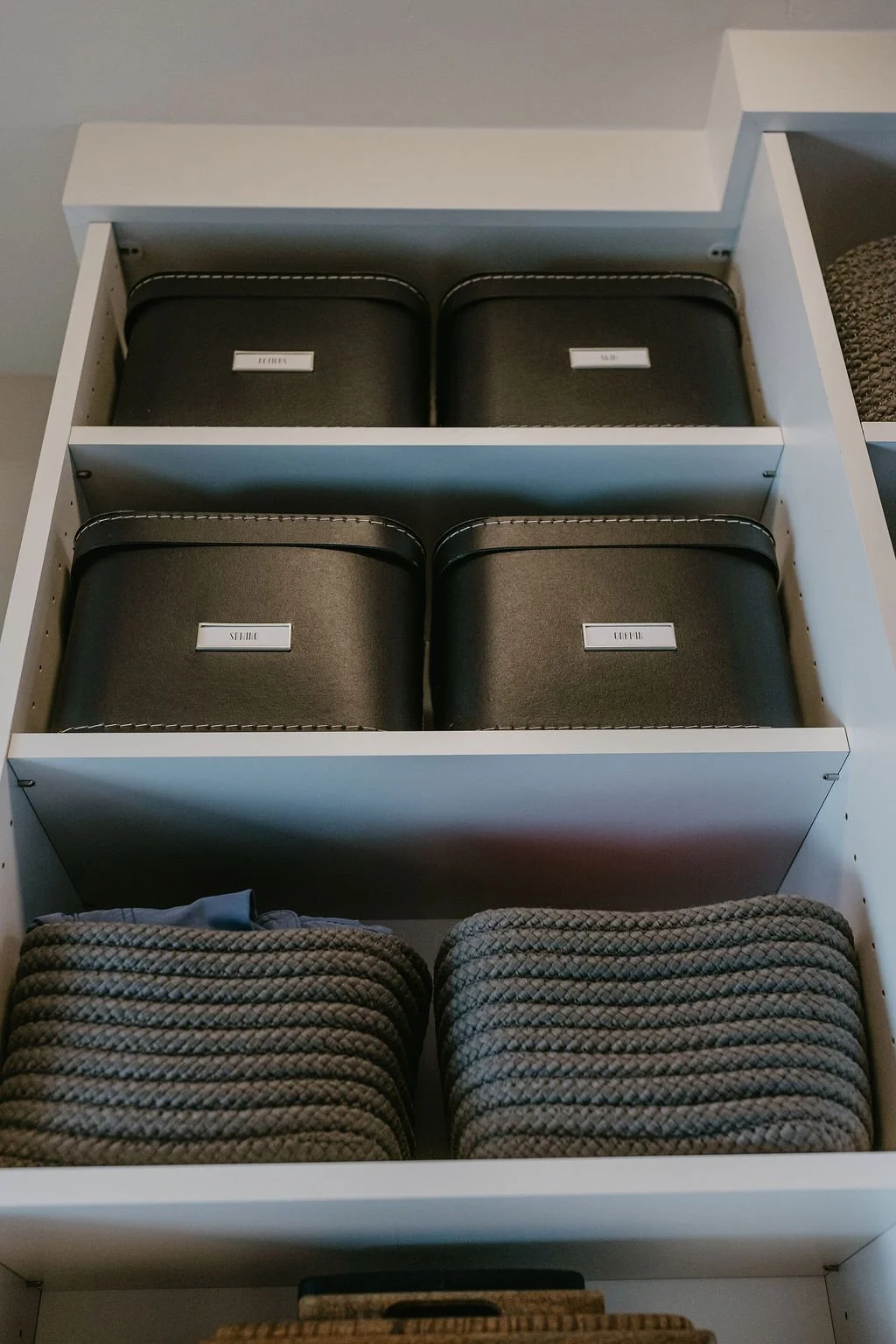 Open drawer containing black zippered cases labeled for shoes, sleeping, casual, and office, along with neatly stacked rolled towels.