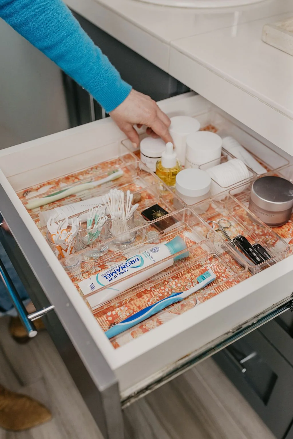 Open bathroom or medical drawer with various health and hygiene items including toothpaste, medicine bottles, q-tips, cotton rolls, and other personal care products.