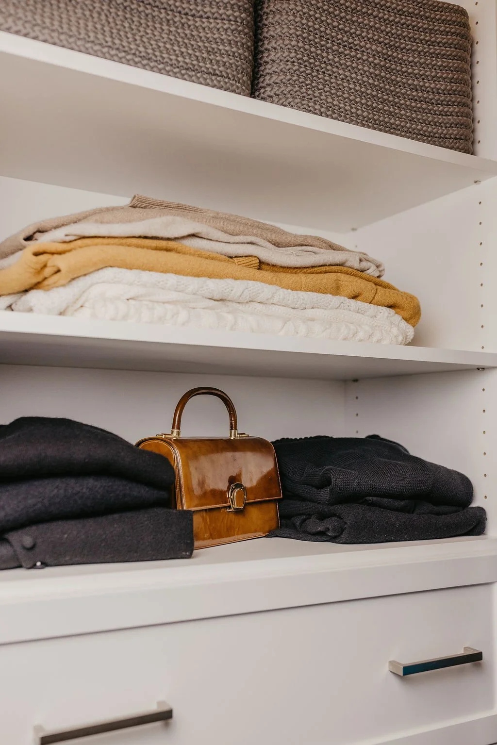 Open white closet with shelves holding folded towels, a purse, and folded clothing.