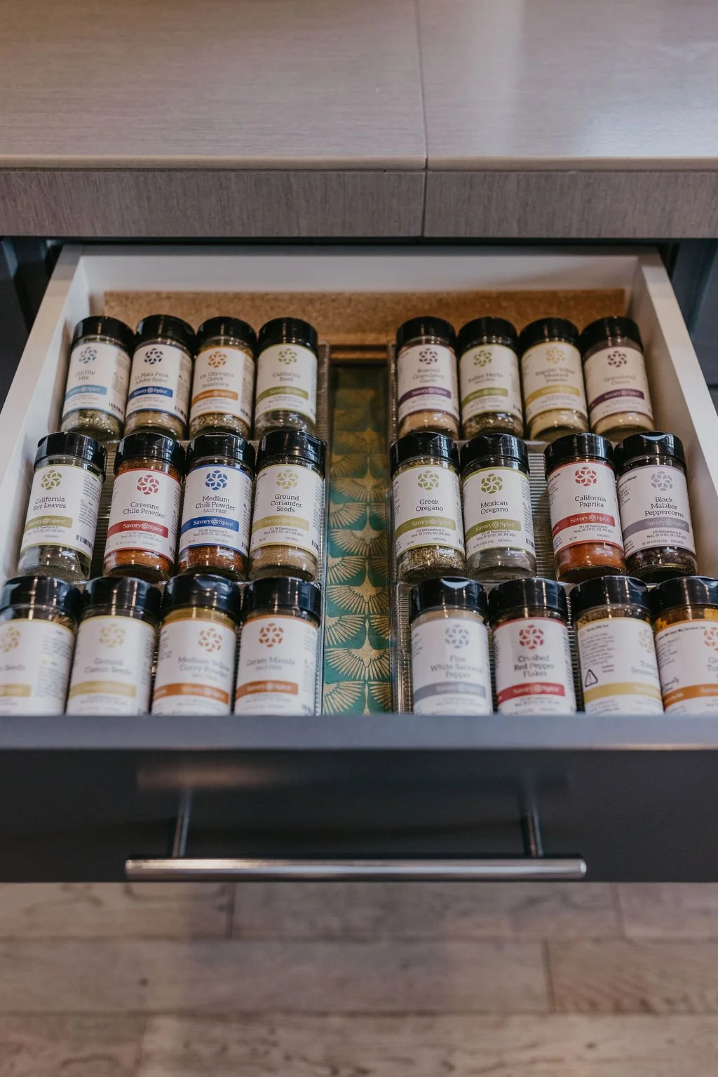 Open kitchen drawer filled with various spice jars labeled with different herbs and seasonings, organized neatly.