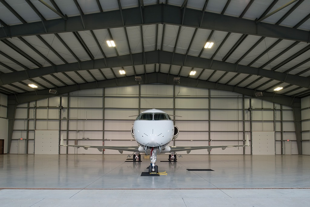 A private jet parked inside a spacious aircraft hangar with a high ceiling and metal walls.