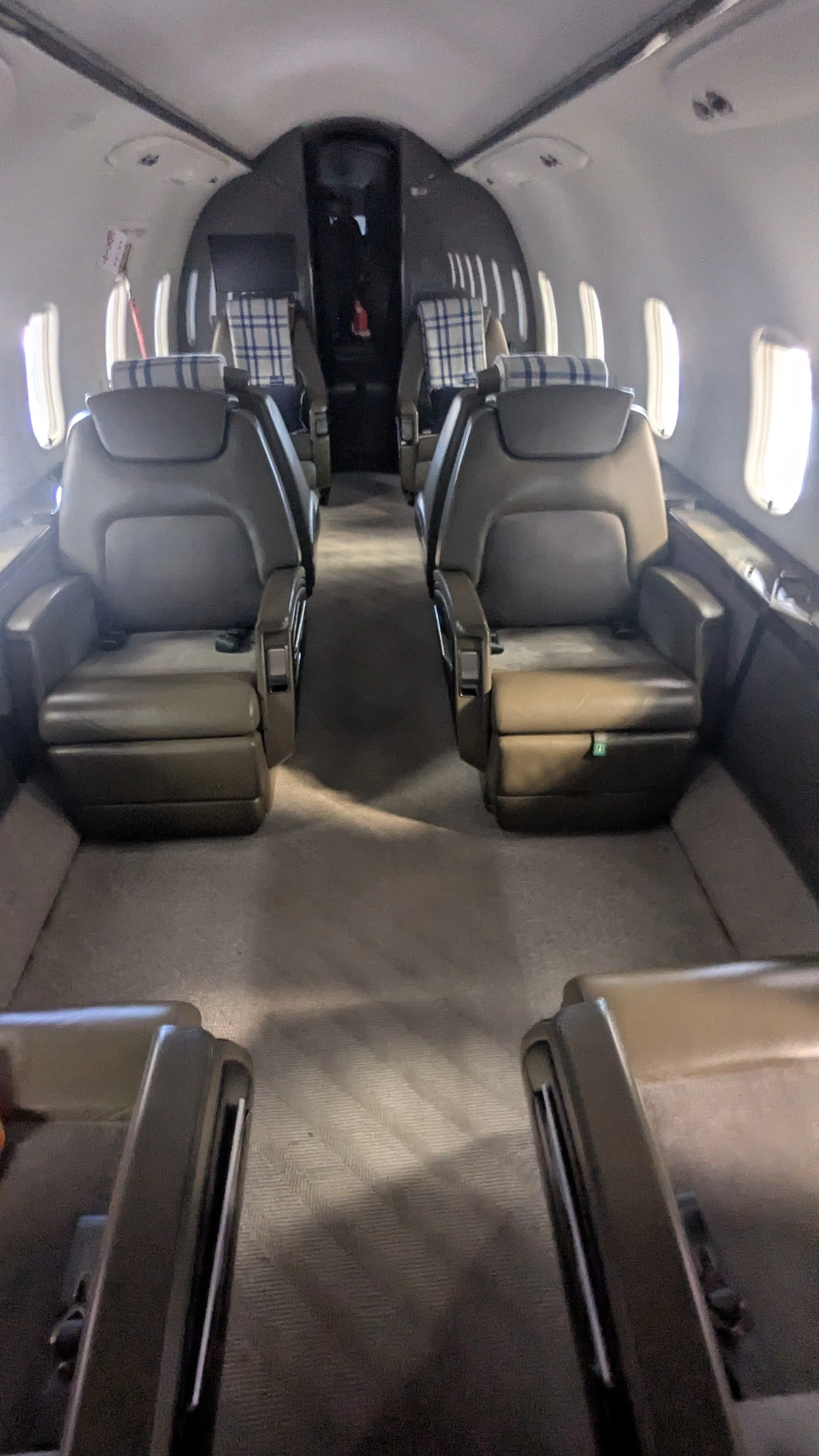 Inside an airplane cabin with several leather seats and plaid headrest covers, viewed from the back.