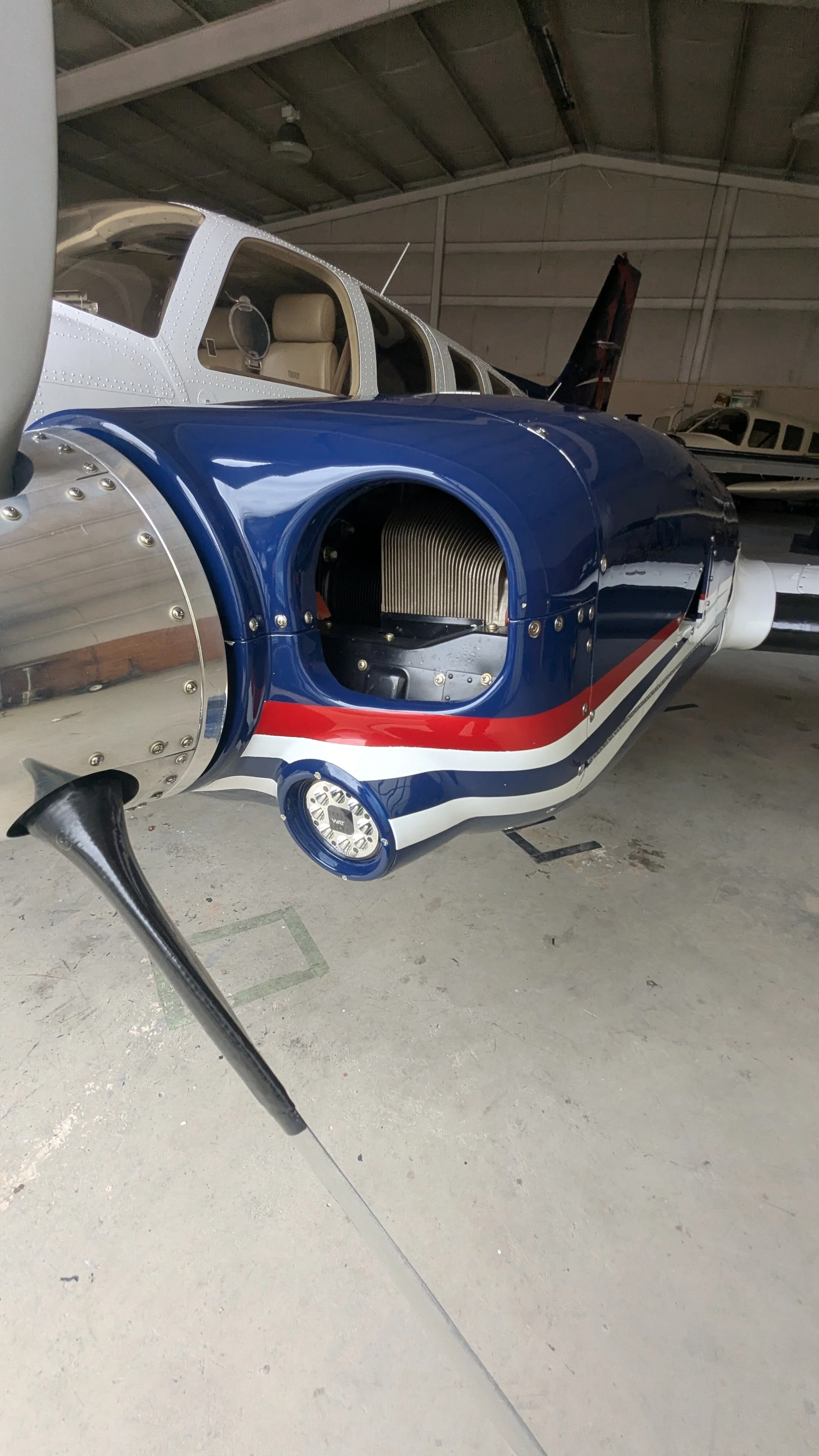 A small aircraft inside a hangar with the nose section open, revealing the engine compartment, with red, white, and blue paint on the fuselage.