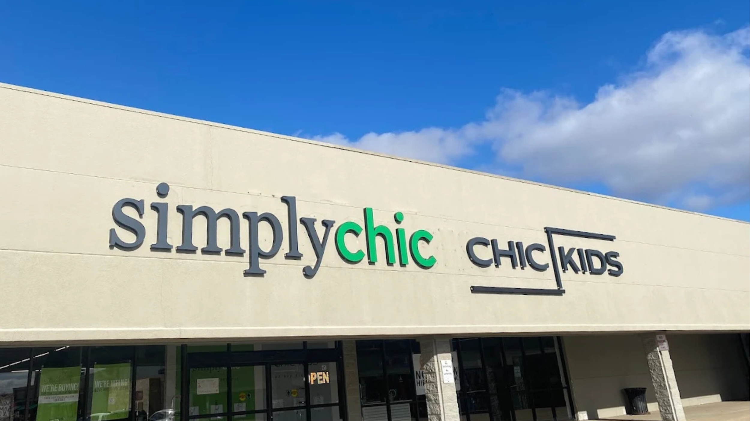 Storefront with signs reading “simply chic” and “CHIC KIDS” for used kids clothing against a tan building and blue sky with clouds.