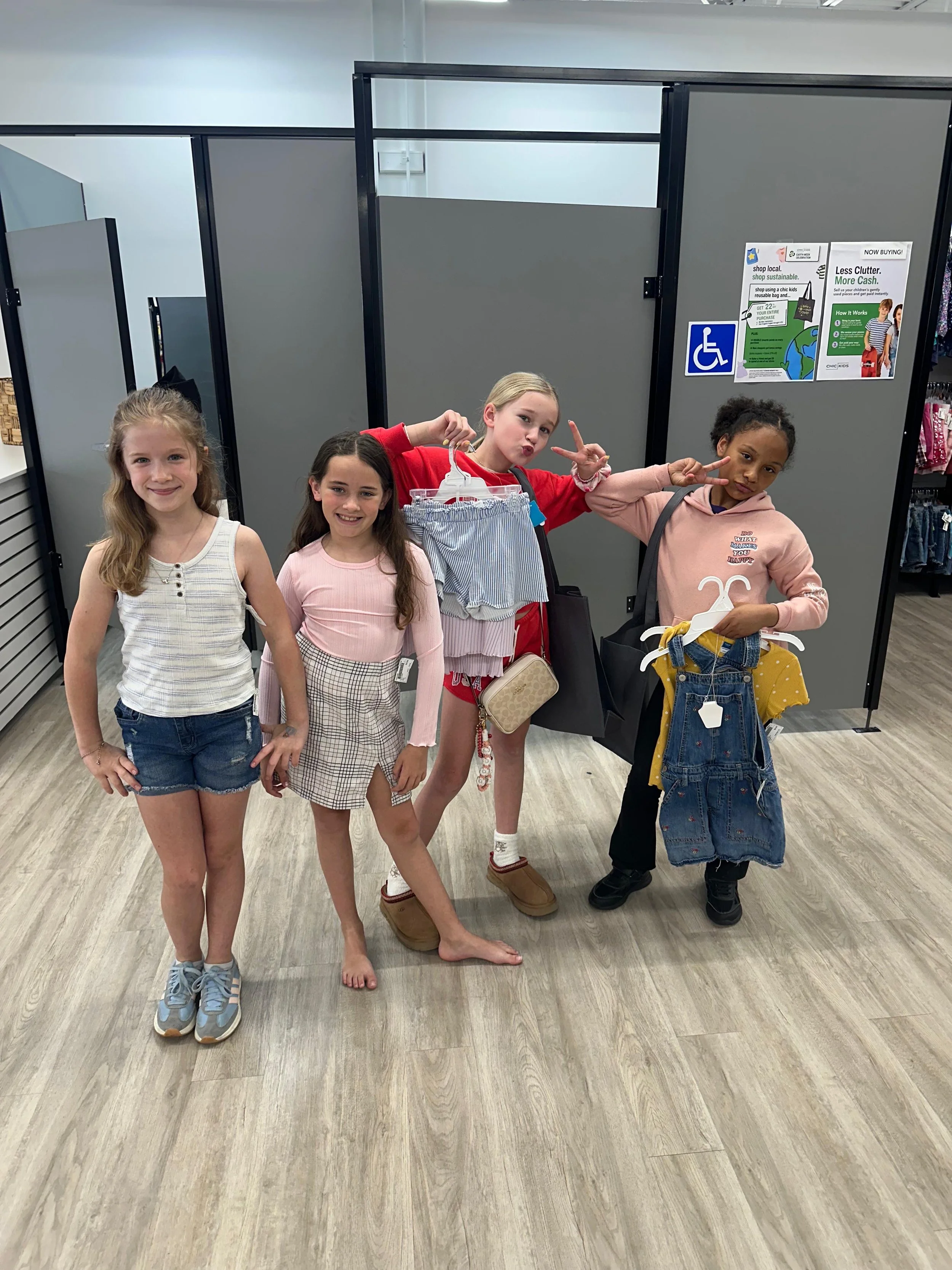 Four young girls stand together holding their gently used children's clothing and smiling.