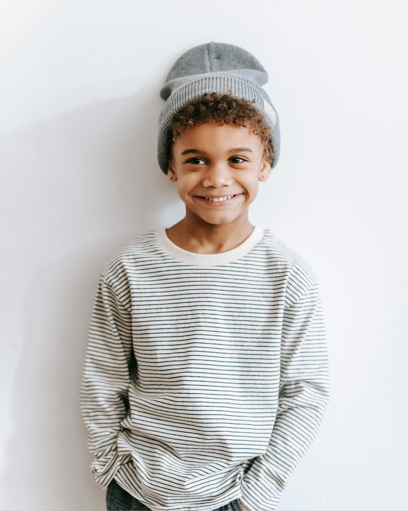 A smiling child wearing resale kids clothing, a striped long-sleeve shirt and gray beanie.