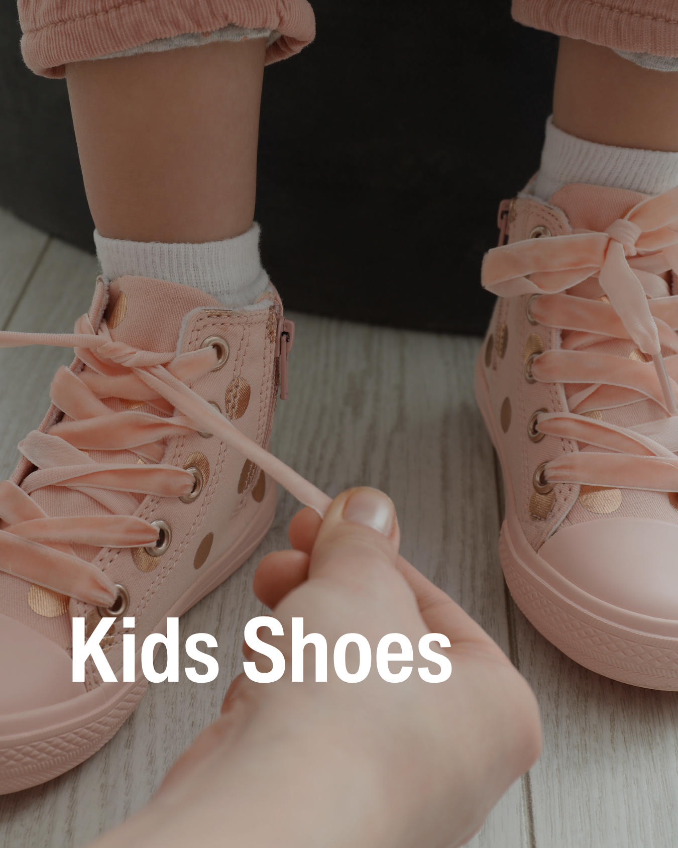 Adult tying pale pink sneakers with gold dots on a child’s feet showcasing the kids resale shoes Chic Kids sells.