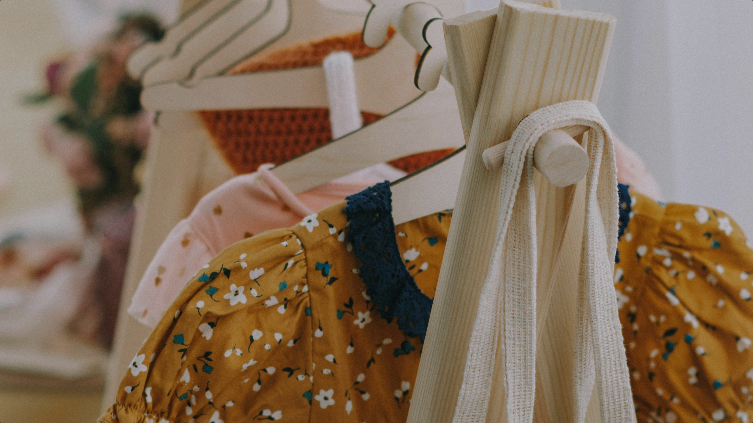 Close-up of wooden hangers holding colorful, patterned secondhand kids clothes and a white tote bag on a wooden rack.