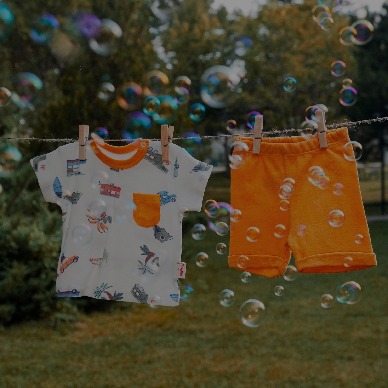 Sustainable children’s t-shirt and shorts on a clothesline outdoors, surrounded by floating soap bubbles in a grassy yard.