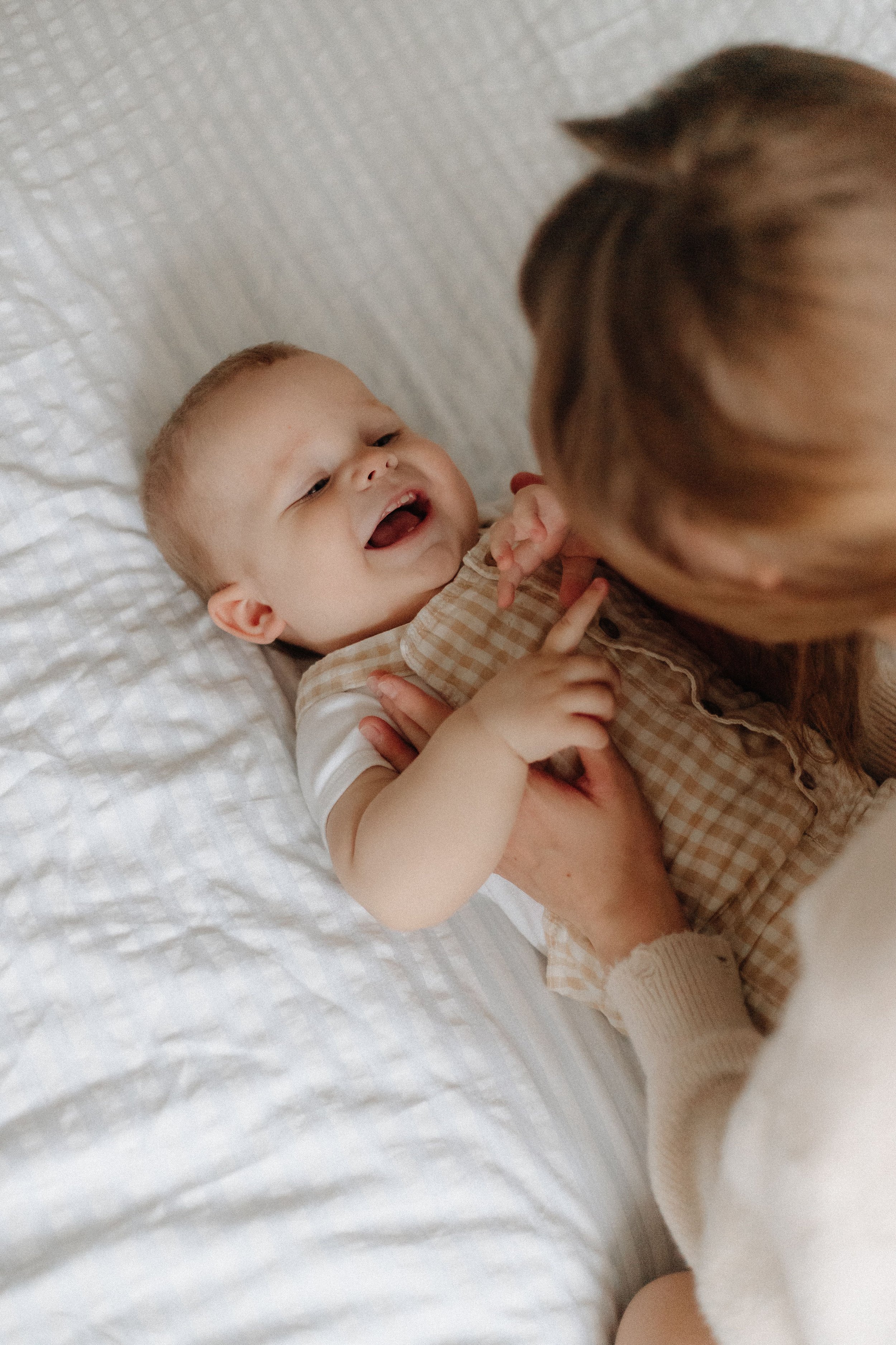 A baby lies on a bed, smiling, while in pre-owned kids clothing.