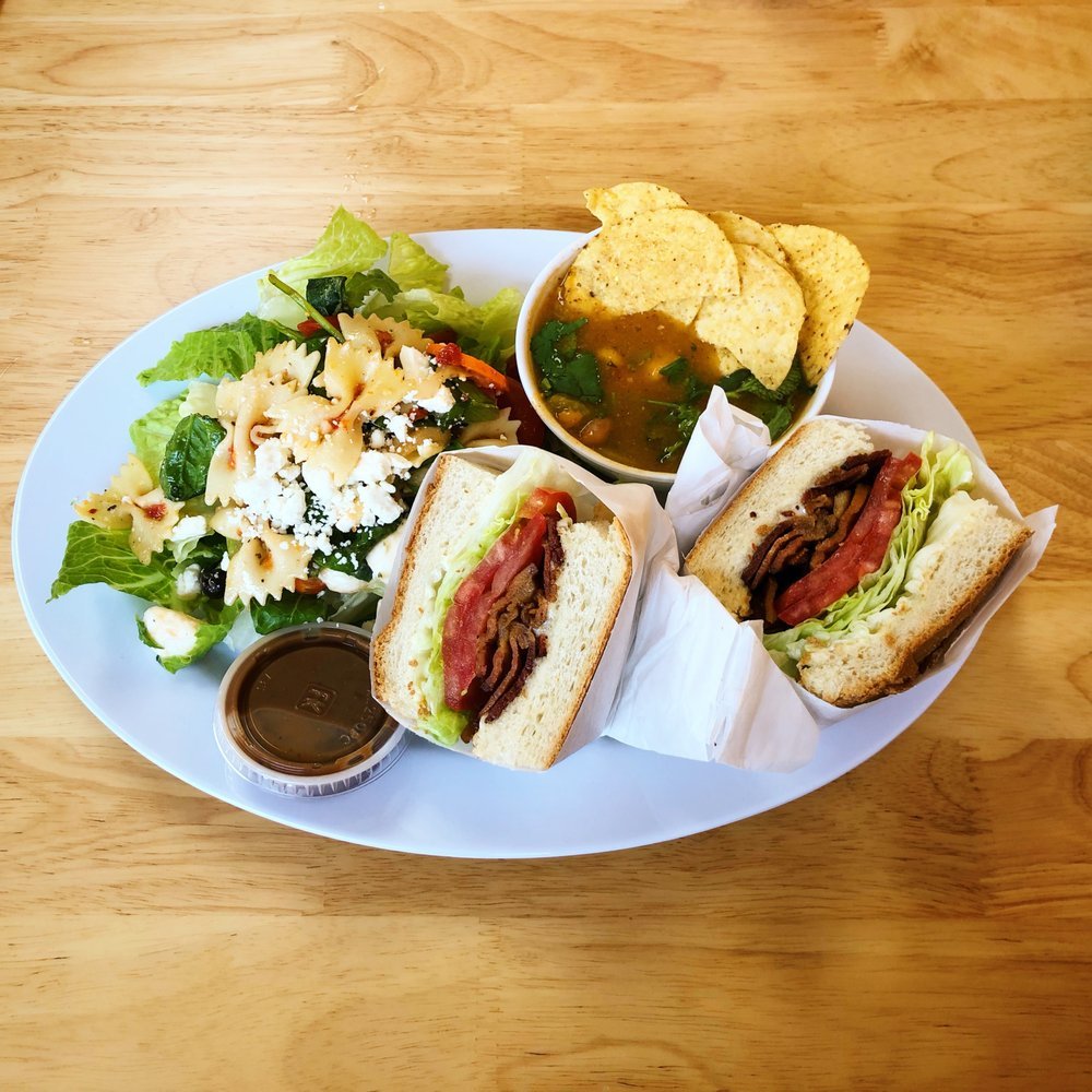 A plate of food with two beef sandwiches, a side salad, a bowl of chili with tortilla chips, and a small container of dipping sauce on a wooden table.