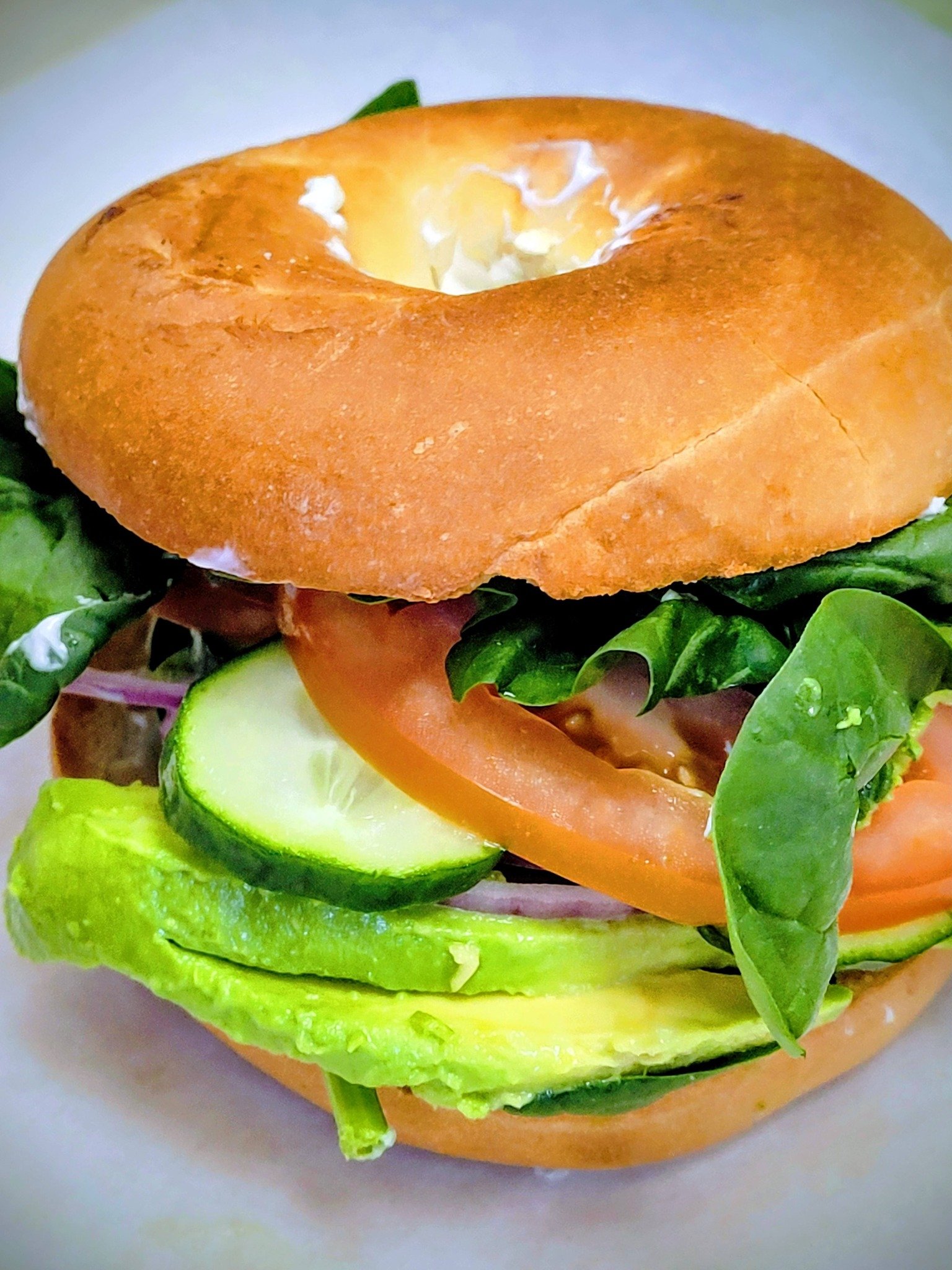 Close-up of a sandwich in a bagel with lettuce, tomato, cucumber, and mayonnaise.