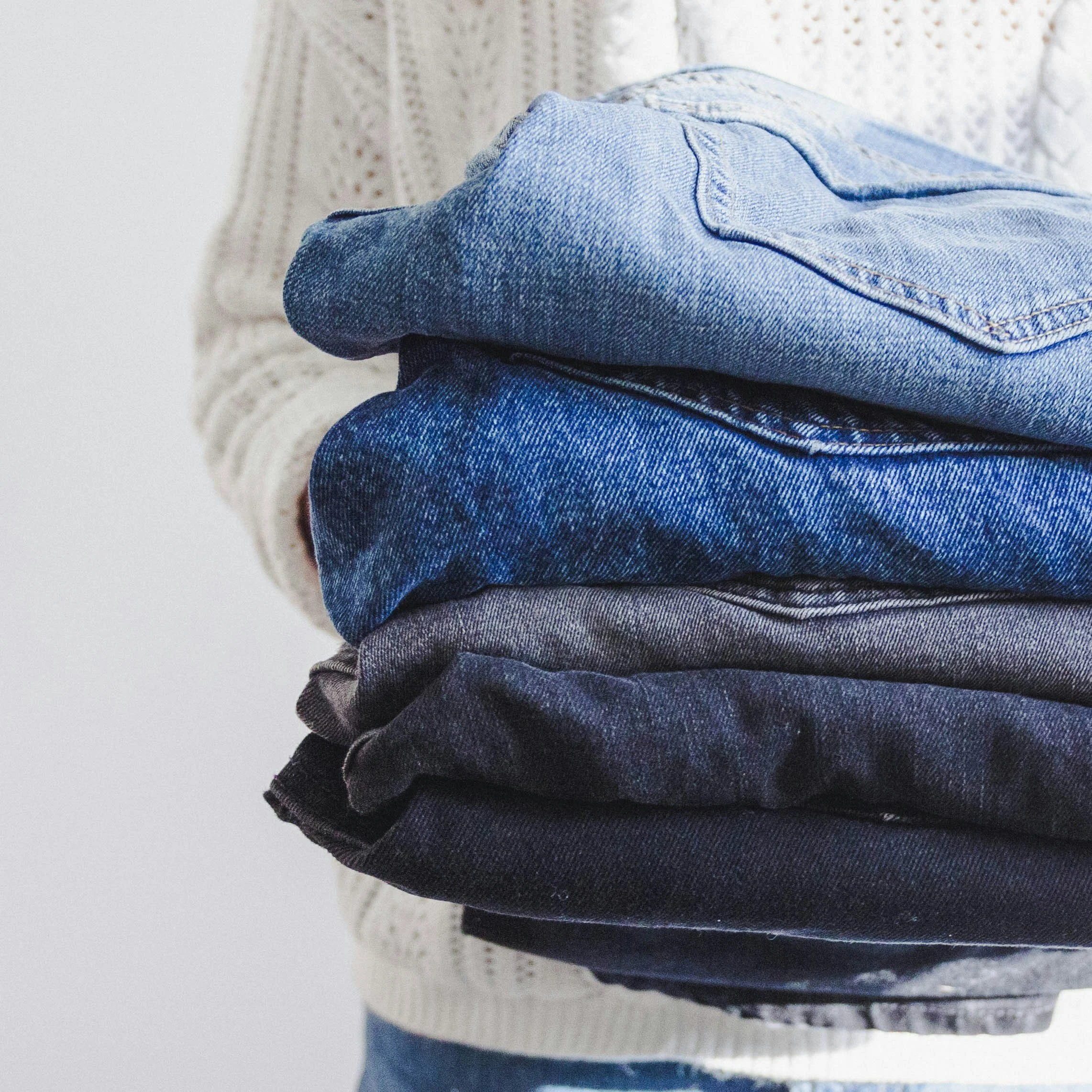Stack of folded jeans in various shades of blue on a white textured surface.