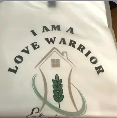 Paper bag with the text 'I am a love warrior' and a logo of a house with a houseplant inside.