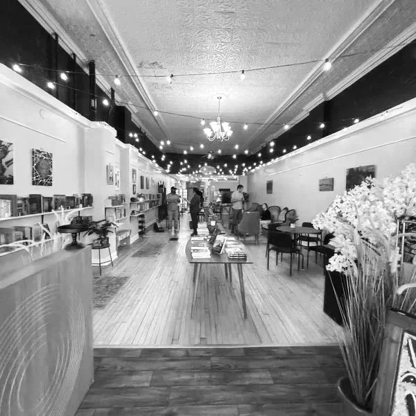 Interior of a boutique or gallery with a long room, bookshelves, artwork on walls, and people browsing.