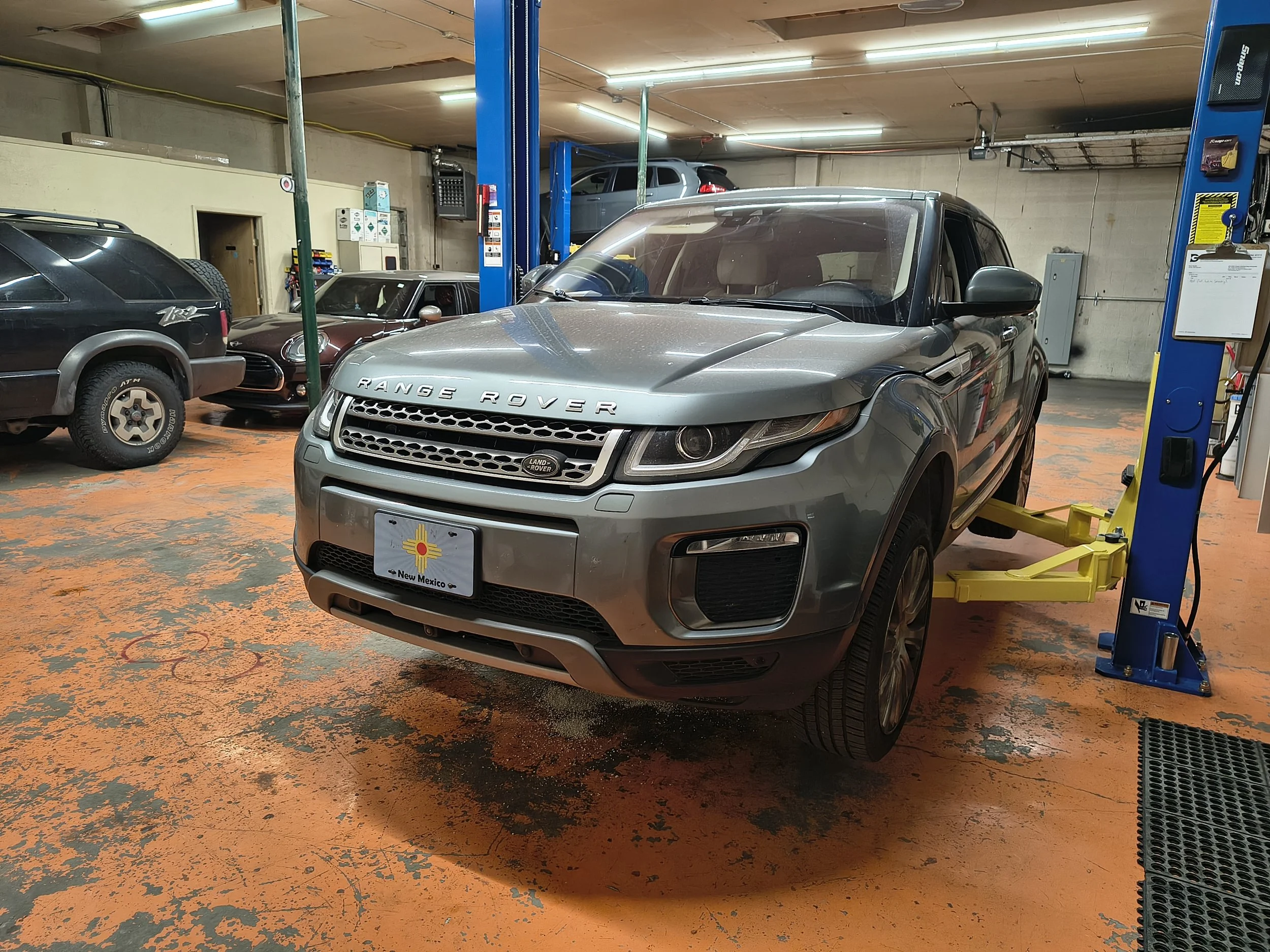 A parking garage with multiple cars, including a silver Range Rover in the foreground, and a car lift with vehicles in the background.