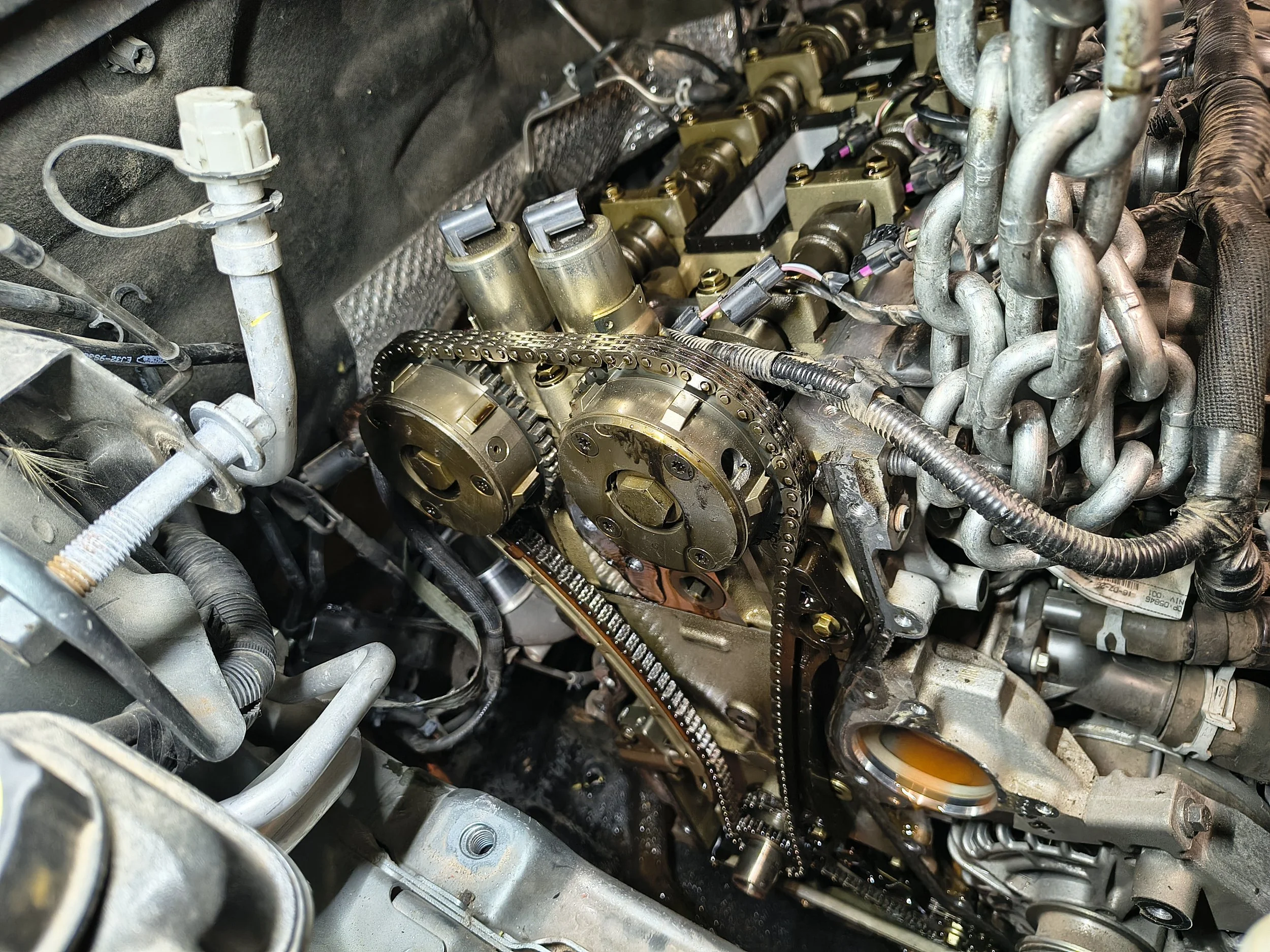 Close-up of a car engine with timing chain, camshafts, and various metal pipes.