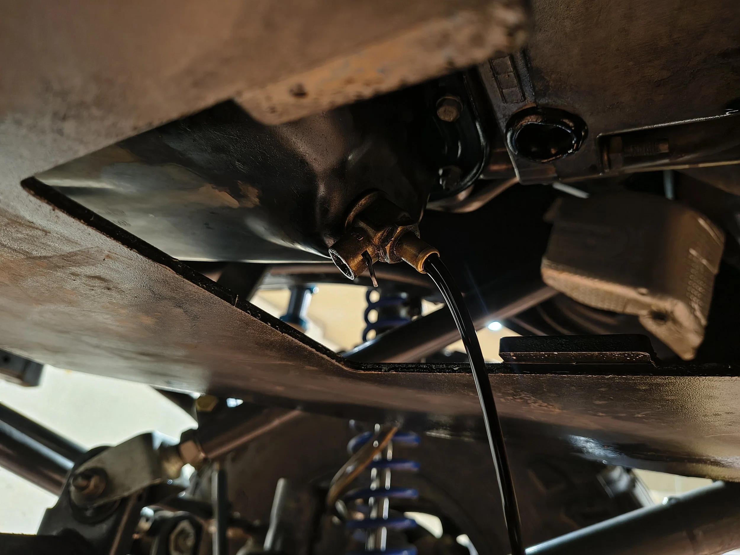 Underneath view of an engine component with oil or fluid being poured into a small opening, possibly during maintenance or repair.