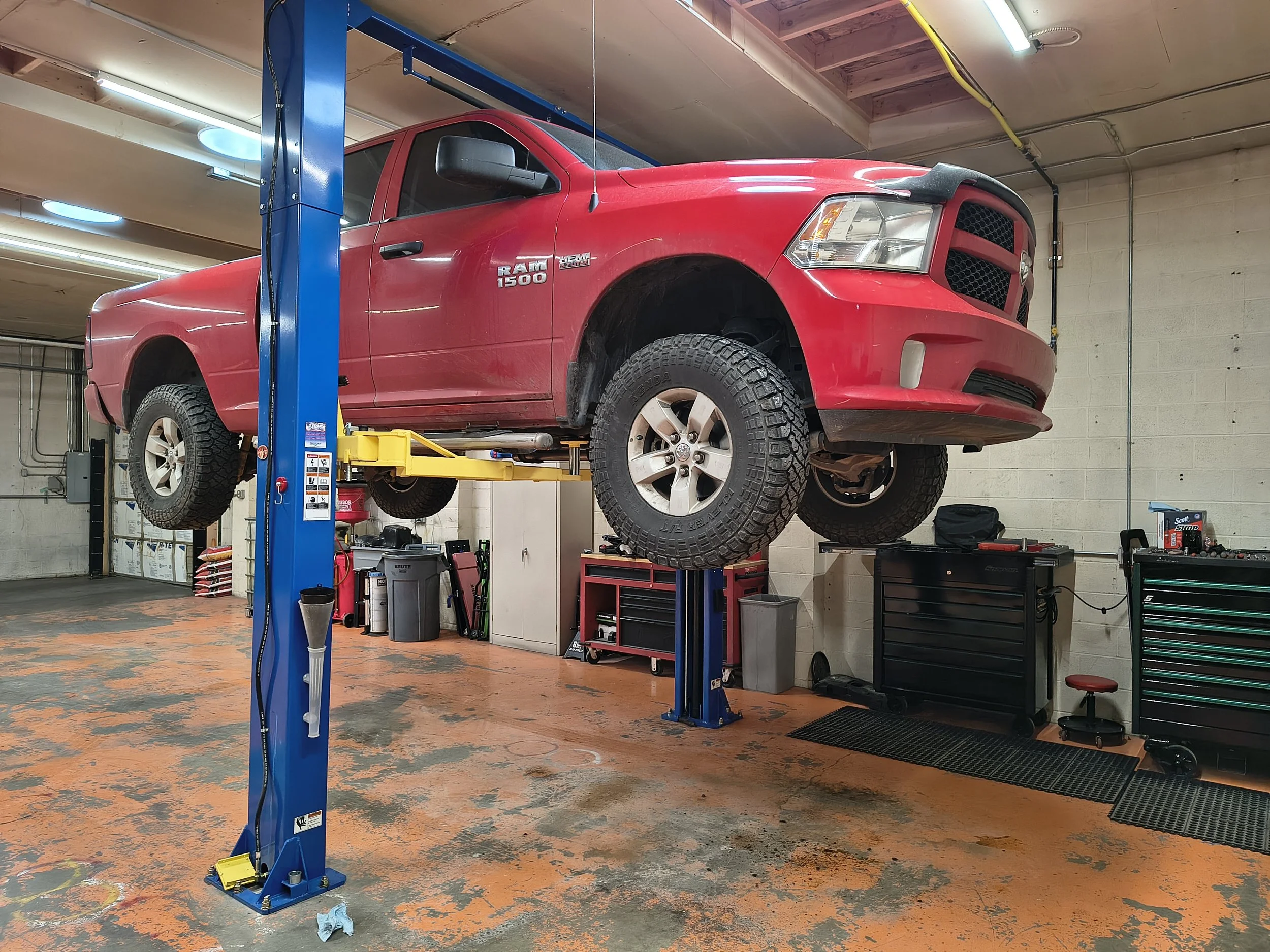 Red Ram 1500 truck lifted on a blue hydraulic lift in an auto repair garage.