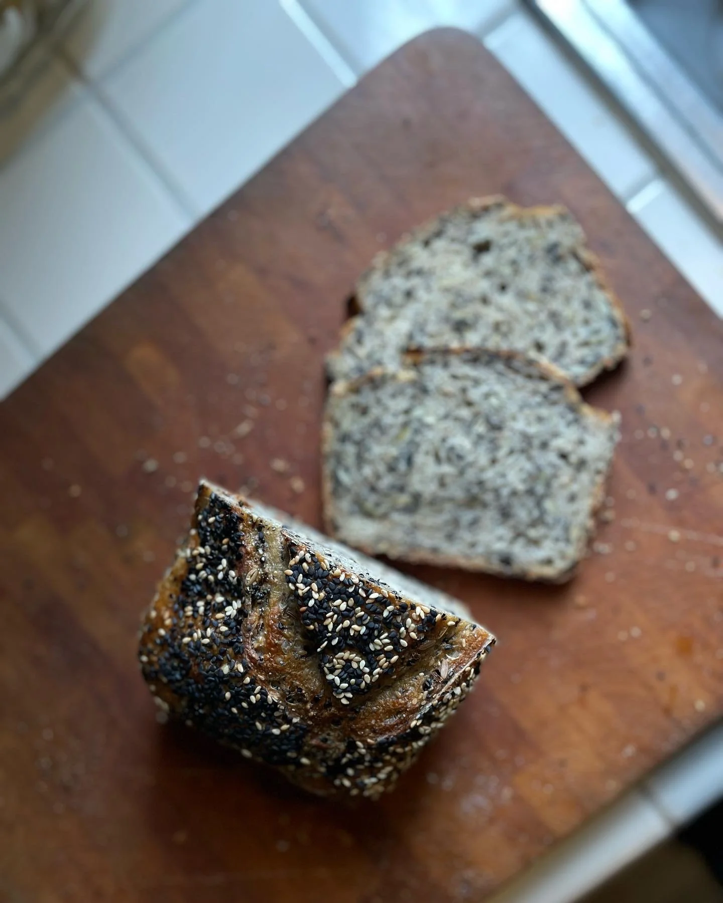 Sliced multigrain bread on a wooden cutting board with an outside crust coated in sesame seeds and black seeds.