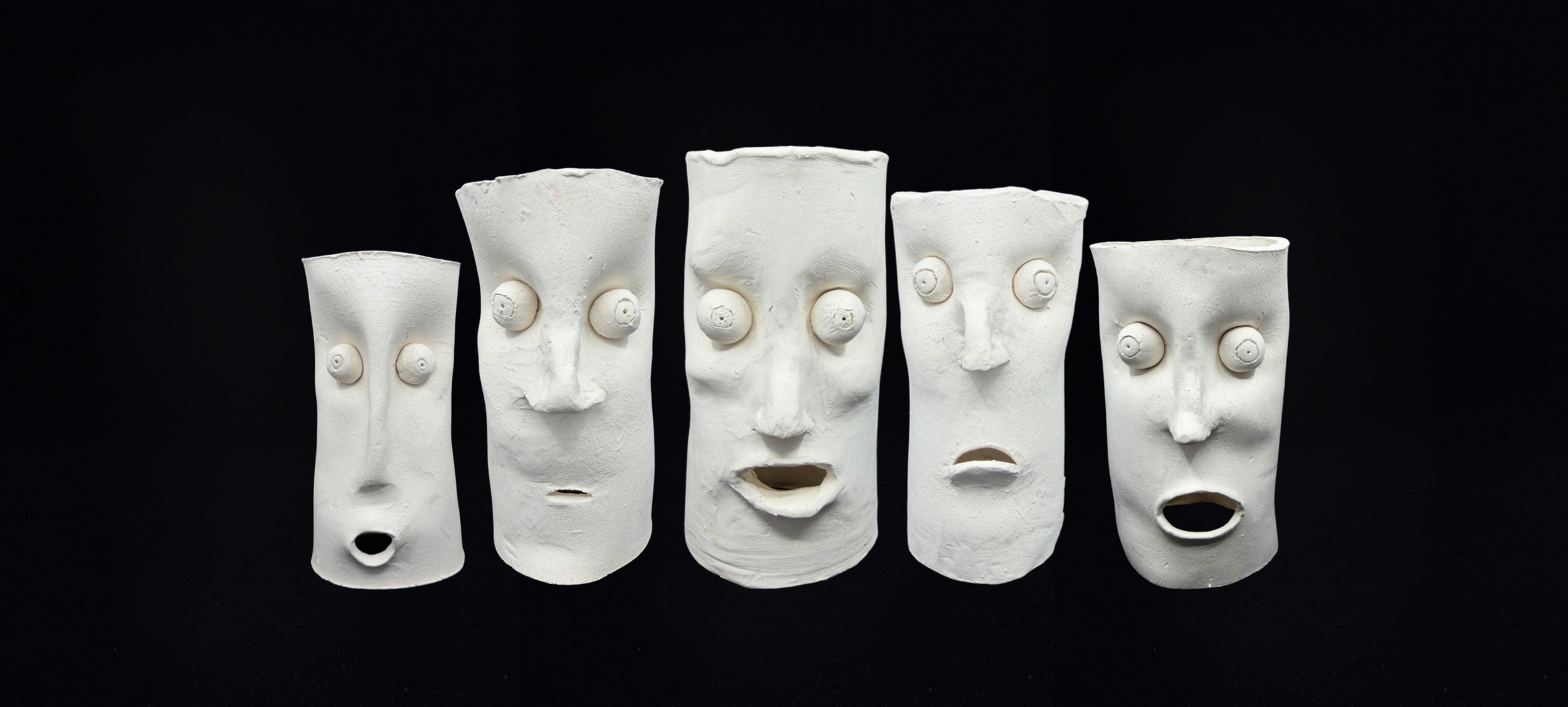 Five white sculptural faces with exaggerated features, eyes, noses, and mouths, set against a black background.