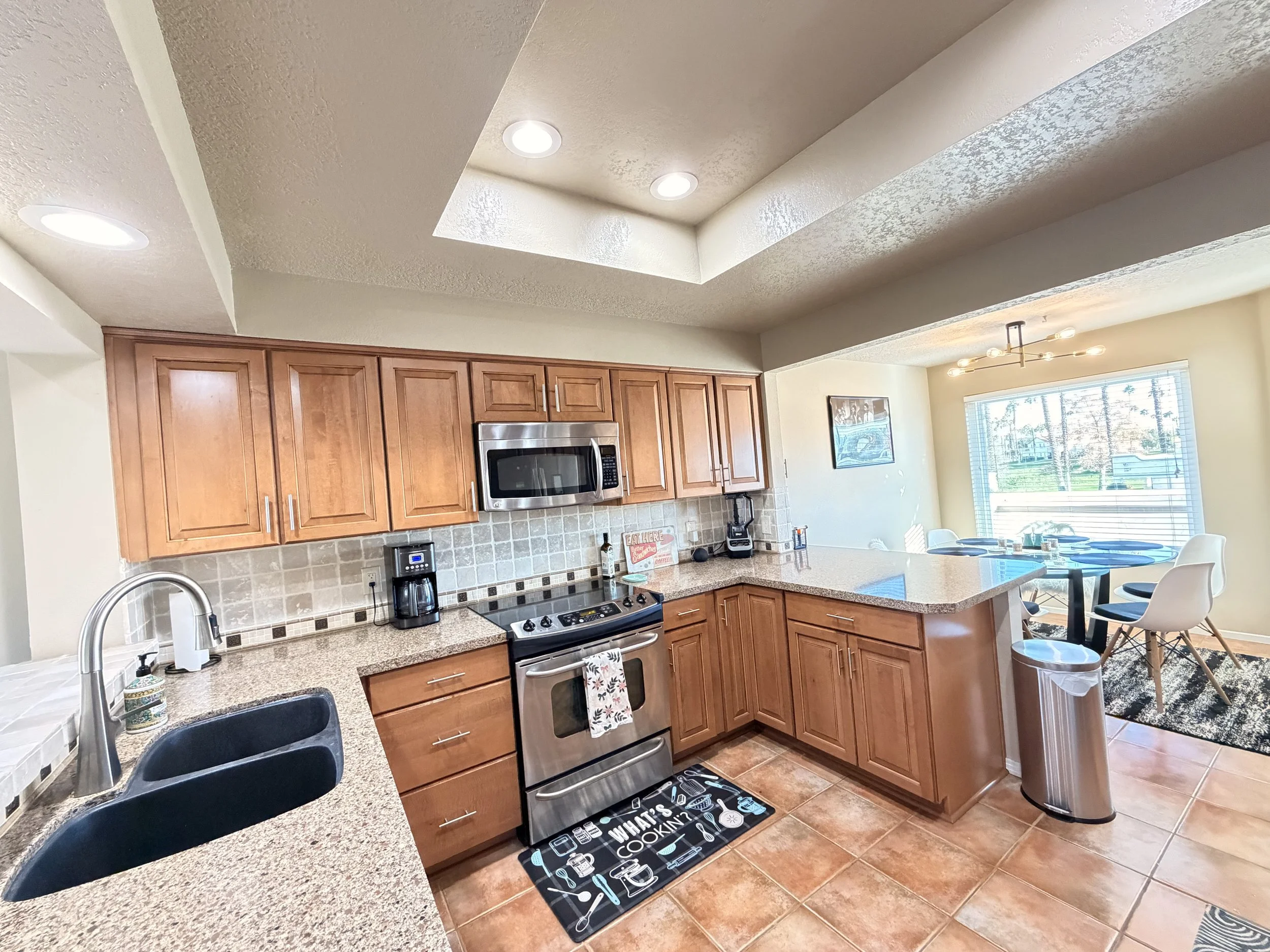 Kitchen with wooden cabinets, granite countertops, stainless steel microwave and stove, tile backsplash, black sink, and over-the-sink window