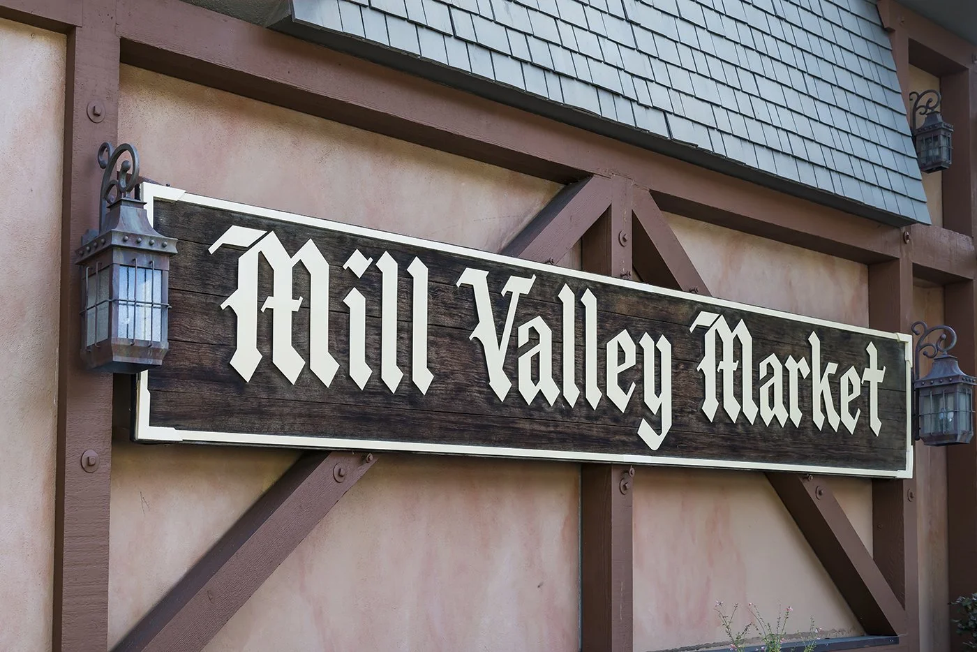 Sign for Mill Valley Market on a wood-paneled building exterior, with decorative lanterns on either side.