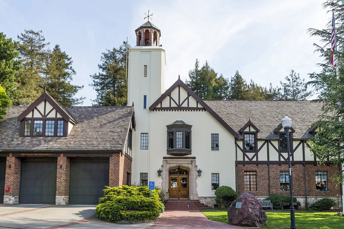 City hall building with a tower, brick and white exterior, surrounded by trees and a small lawn.