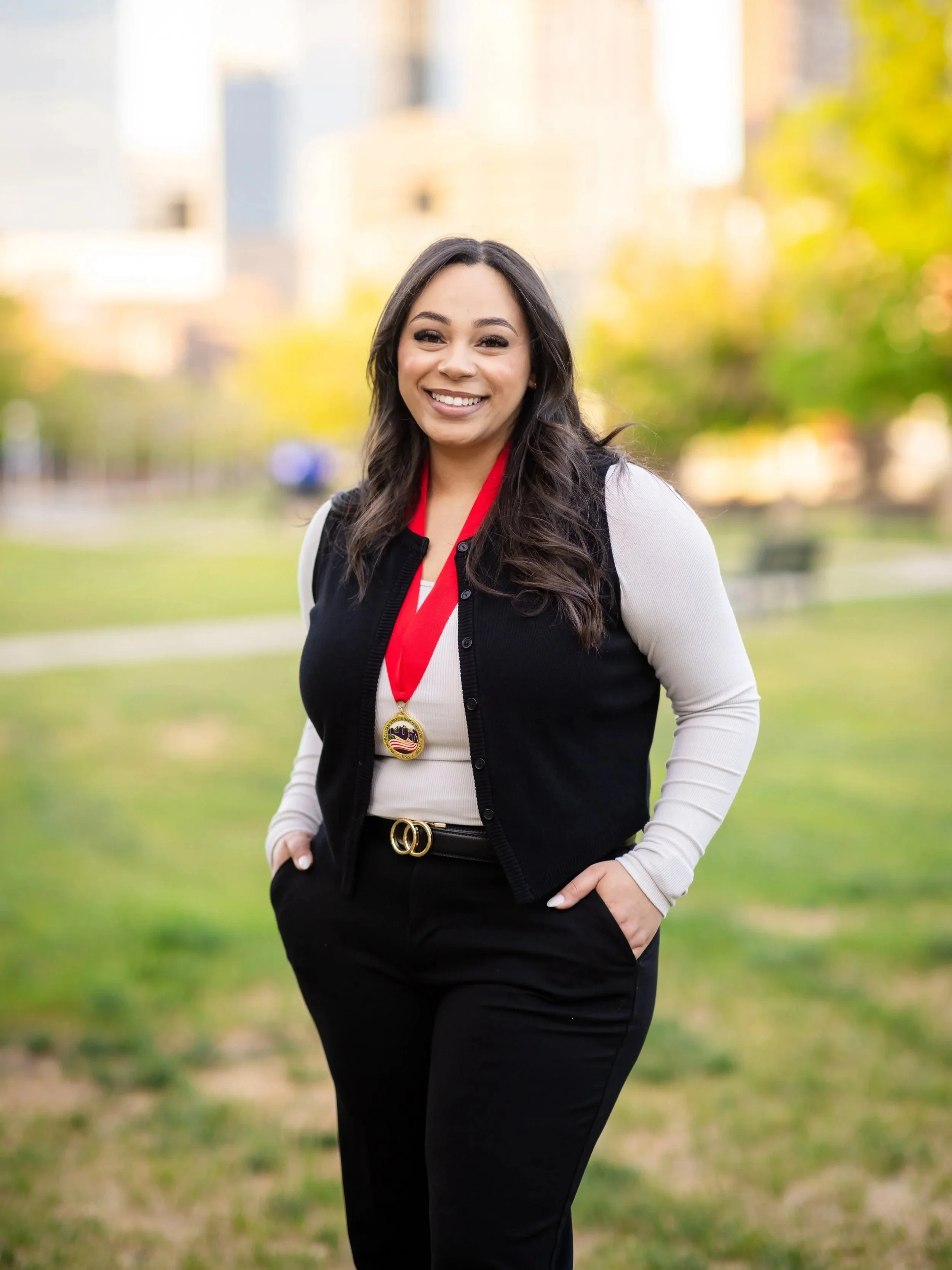 Woman smiling outside in a park with a gold medal hanging from a red ribbon around her neck.