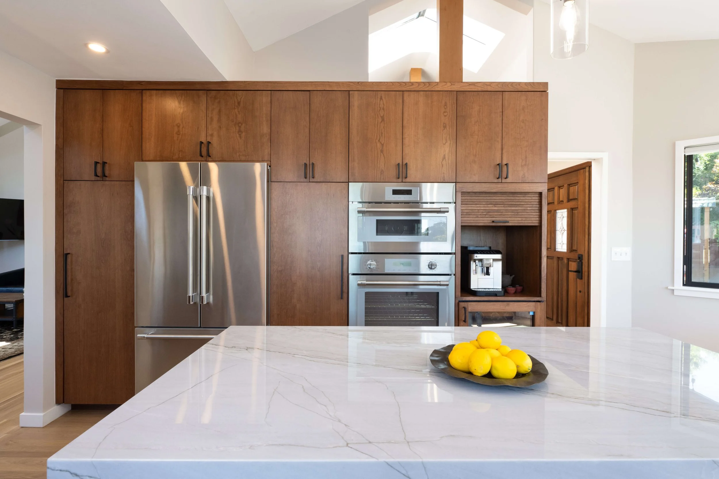 Kitchen with wooden cabinets, stainless steel refrigerator, built-in oven, and a white marble island with a bowl of bright yellow lemons.