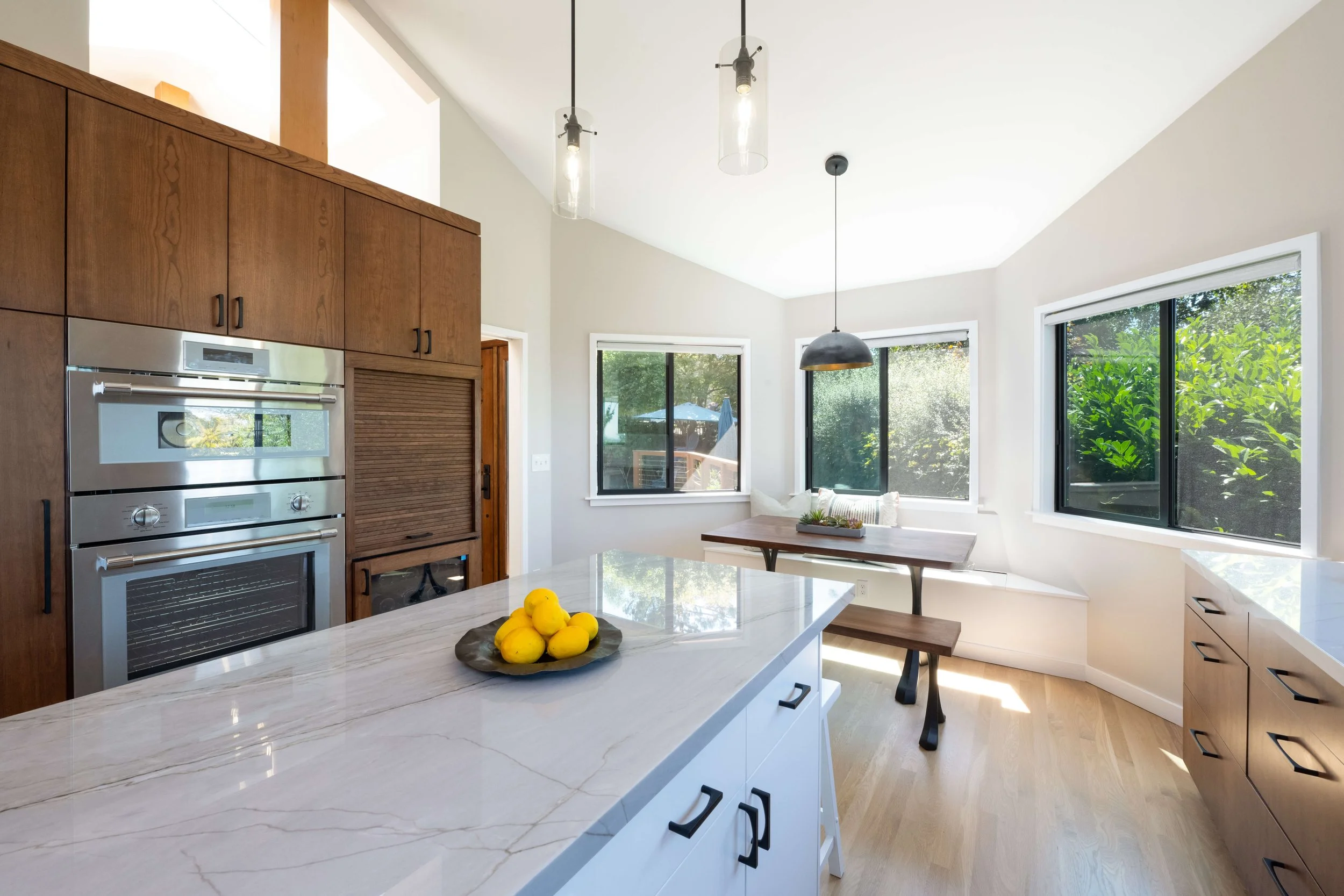Bright, modern kitchen with large windows, white cabinetry, a central island with a bowl of lemons, and wooden accents.