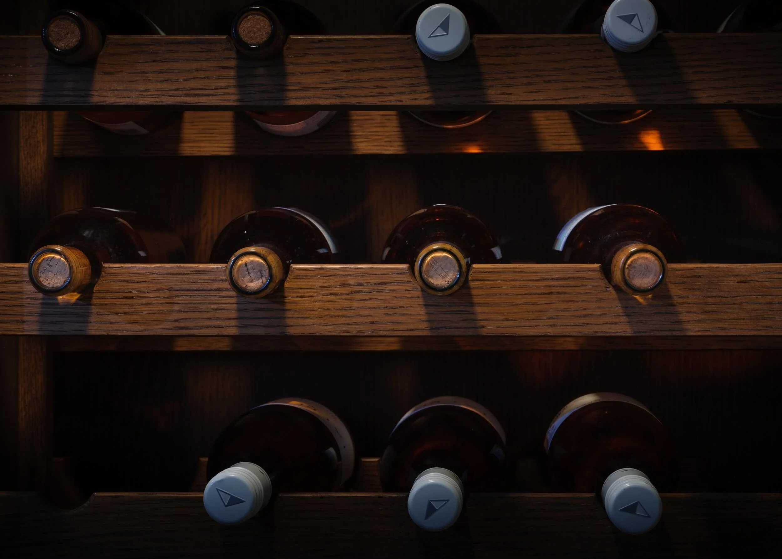 Top view of a wooden wine rack with bottles stored horizontally and bottle caps with a triangle logo visible on some bottles.