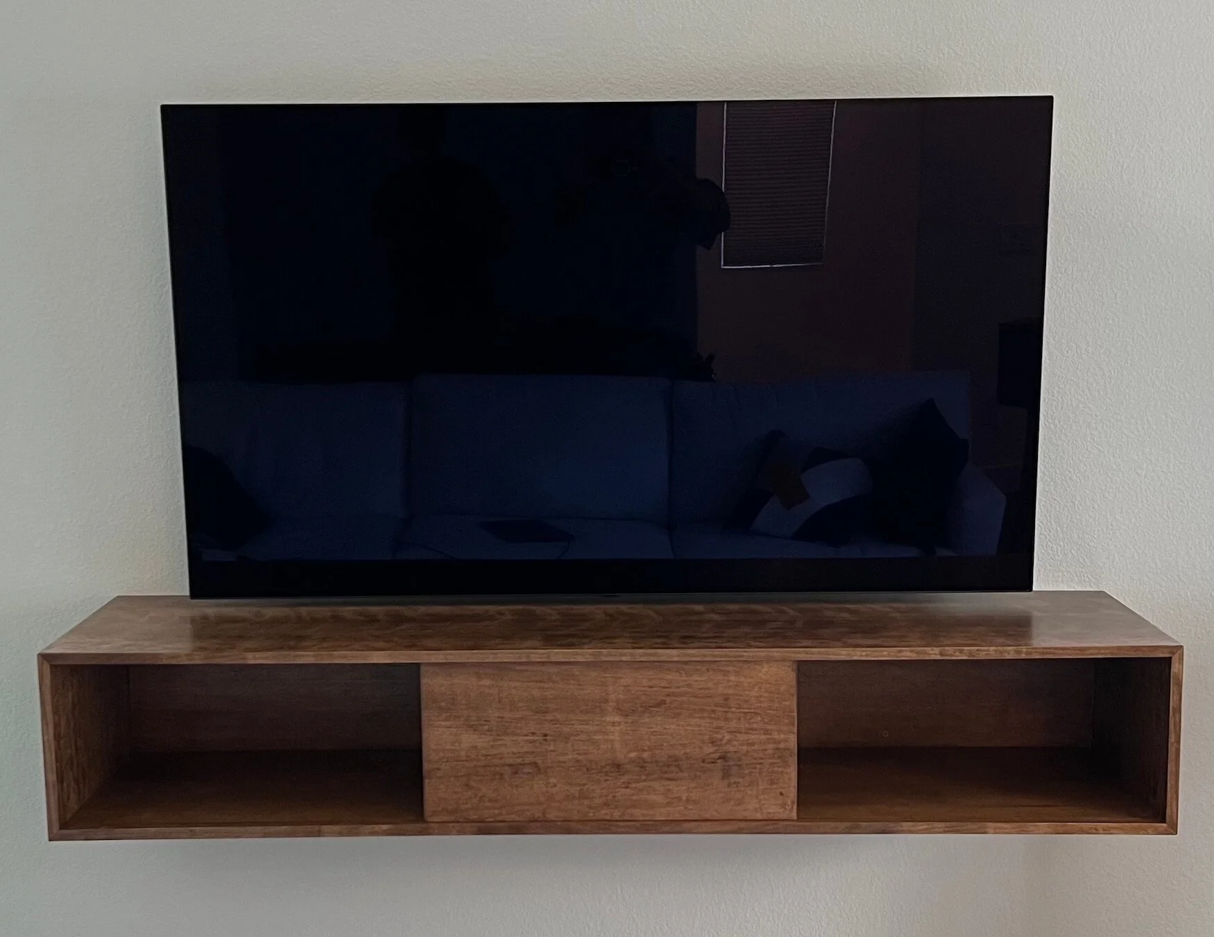 Flat-screen television turned off on a wooden TV stand against a beige wall.