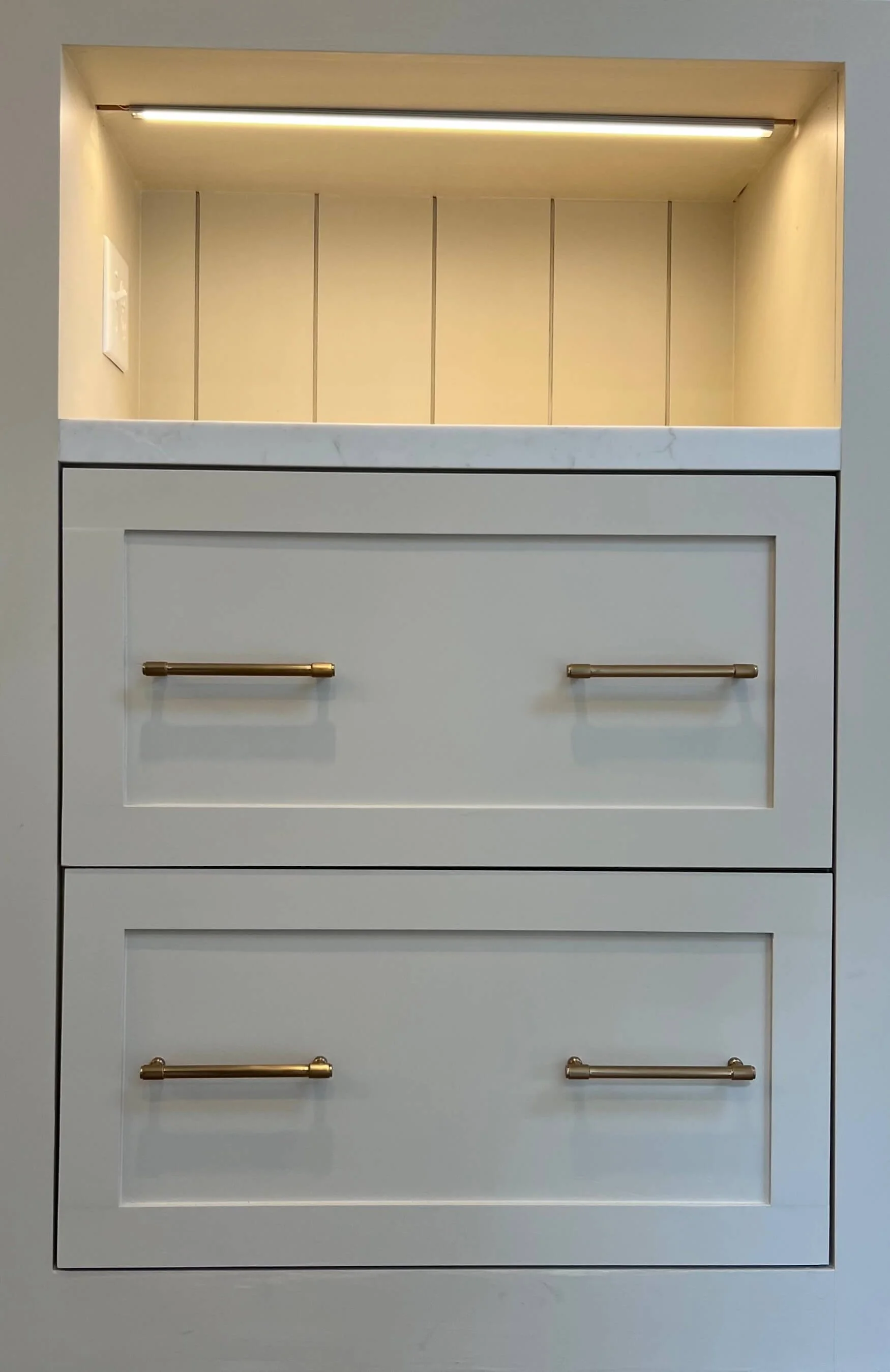 White drawer unit with five drawers, gold handles, and an open upper display space illuminated by a light.