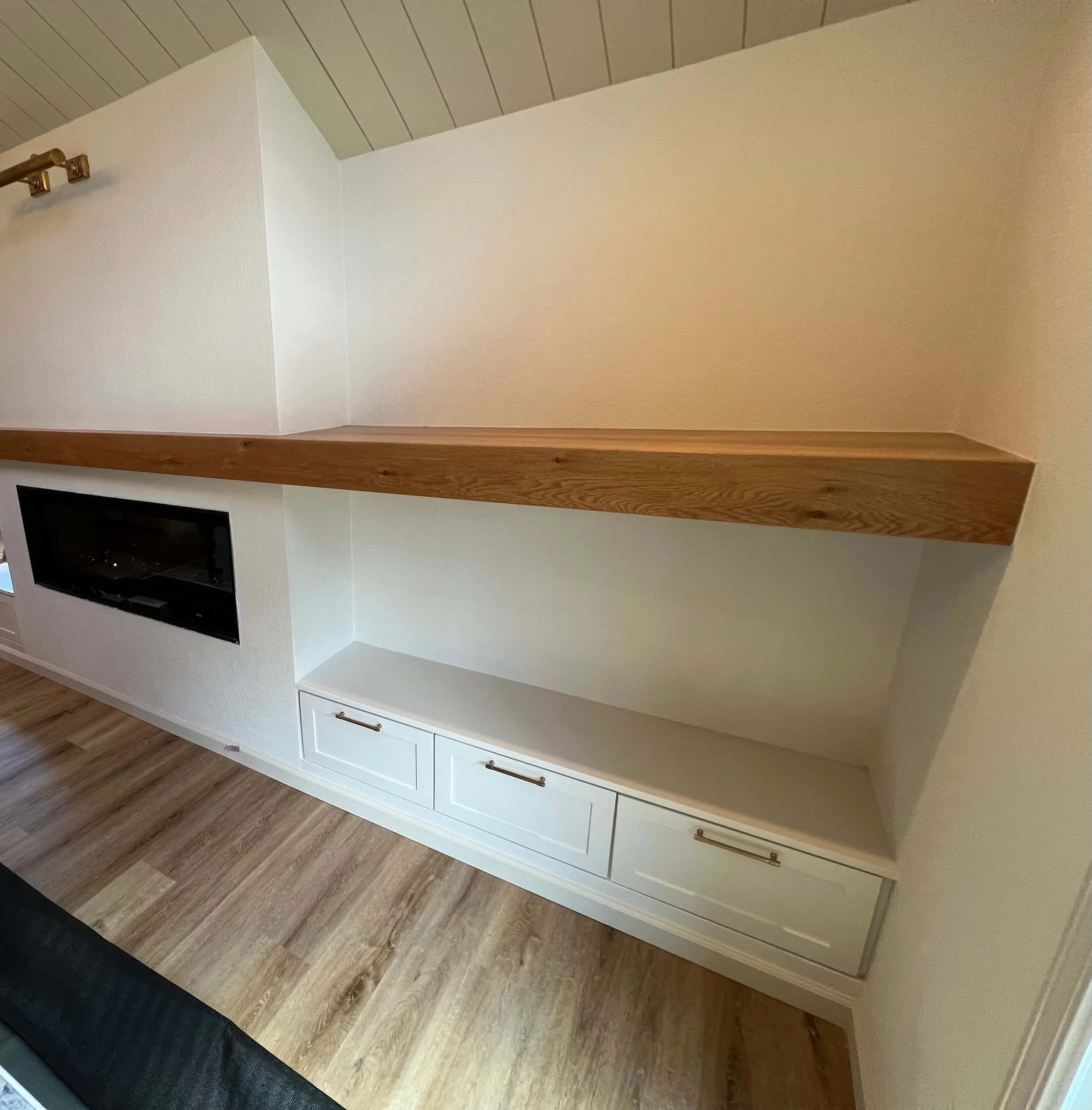 White built-in cabinet with brass handles, topped with a wooden surface, in a room with wood flooring.