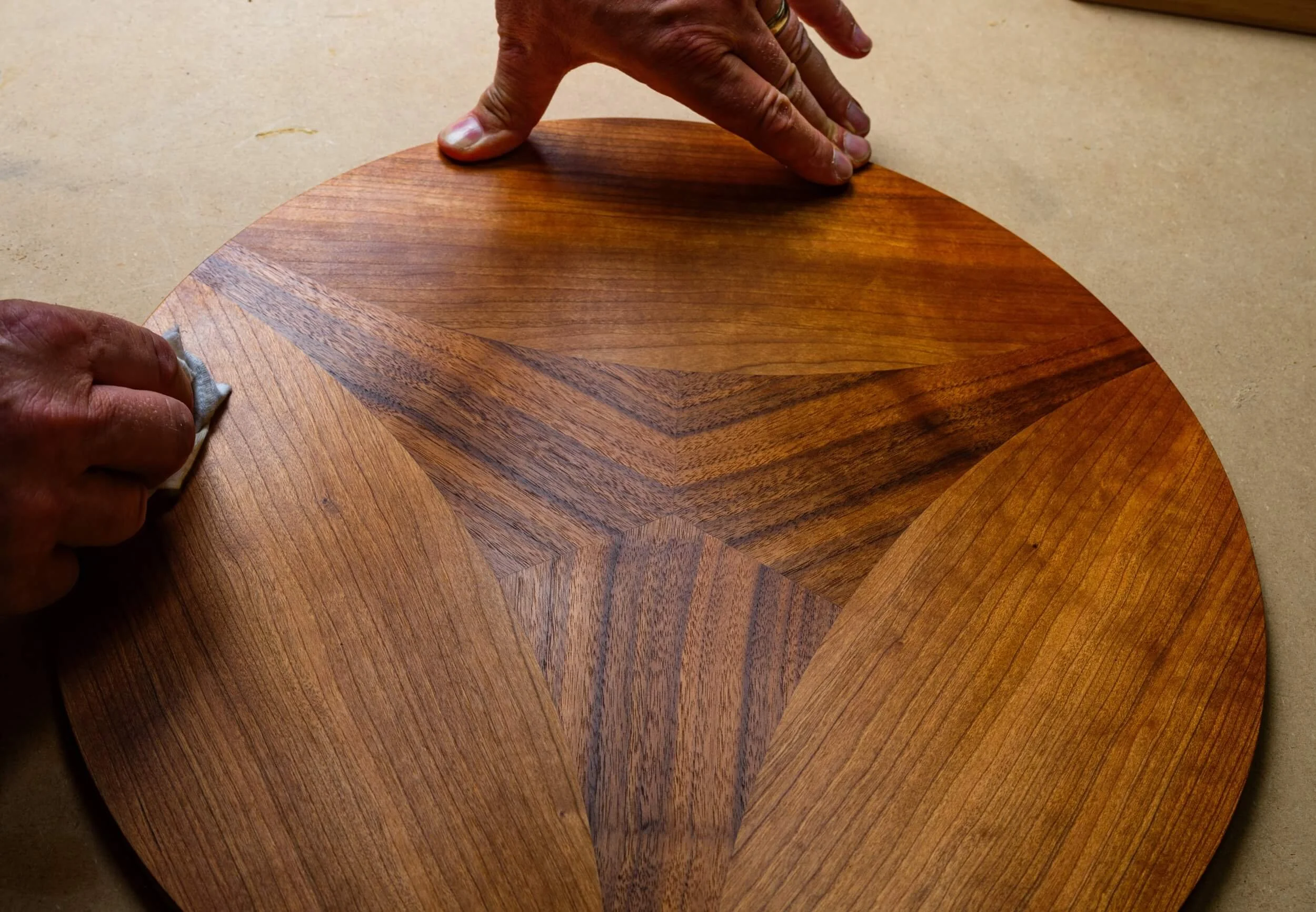 Person polishing a wooden piece of furniture with a cloth, focusing on hands and the wood surface.