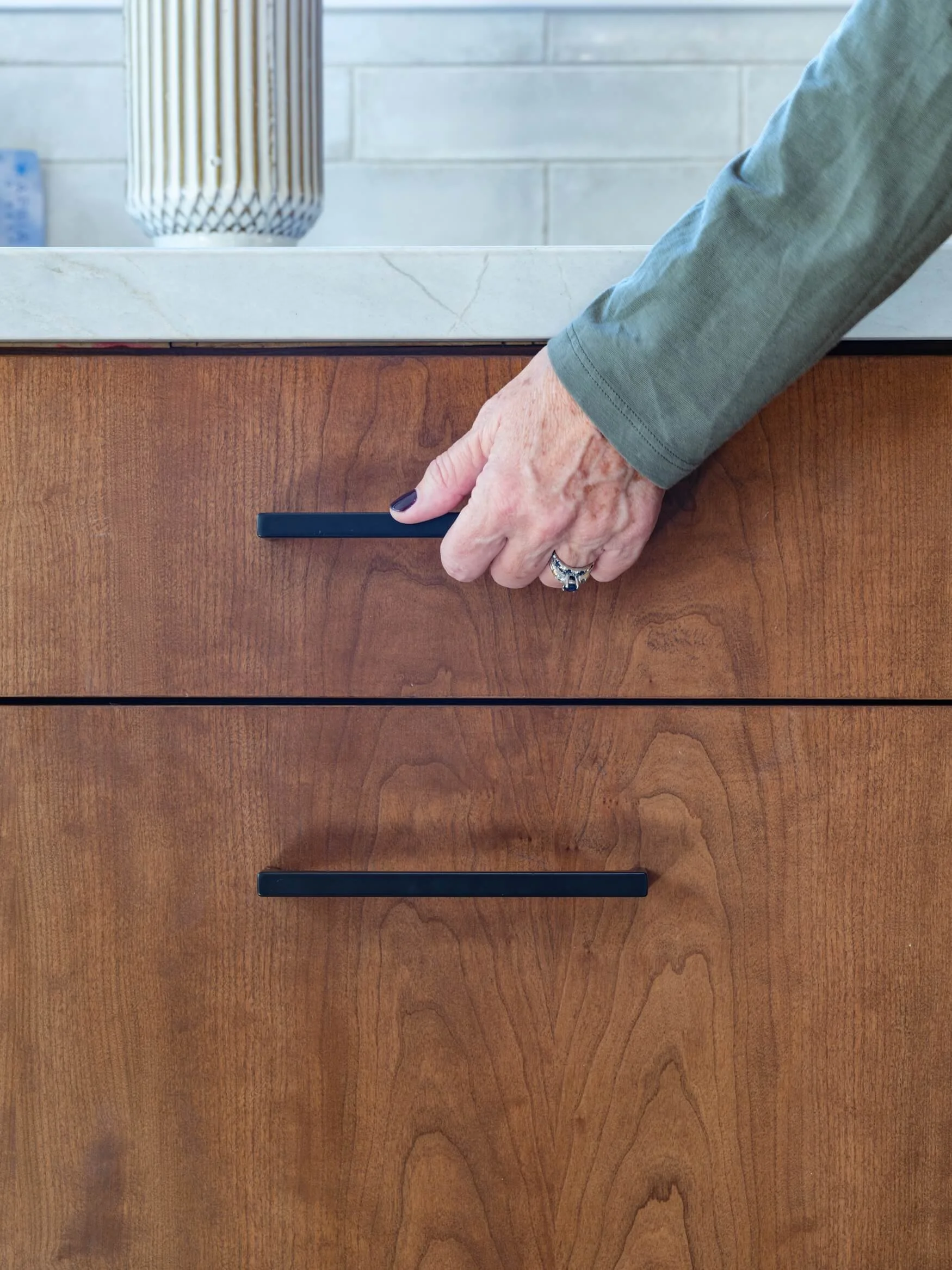 A person's hand with black nail polish and ring on finger is moving a drawer handle on a wooden desk or table.