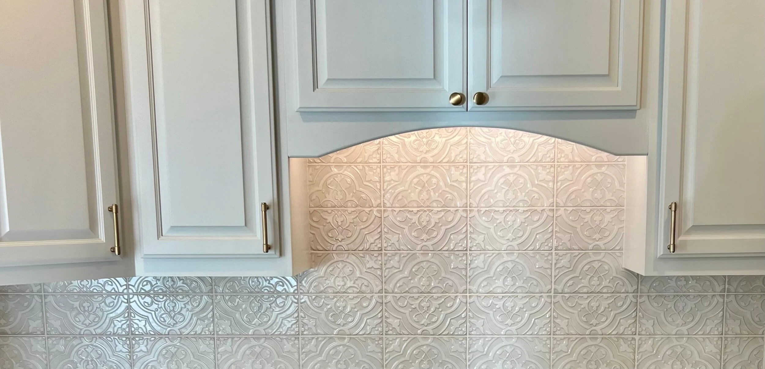 White kitchen cabinets with gold handles above decorative white tile backsplash.