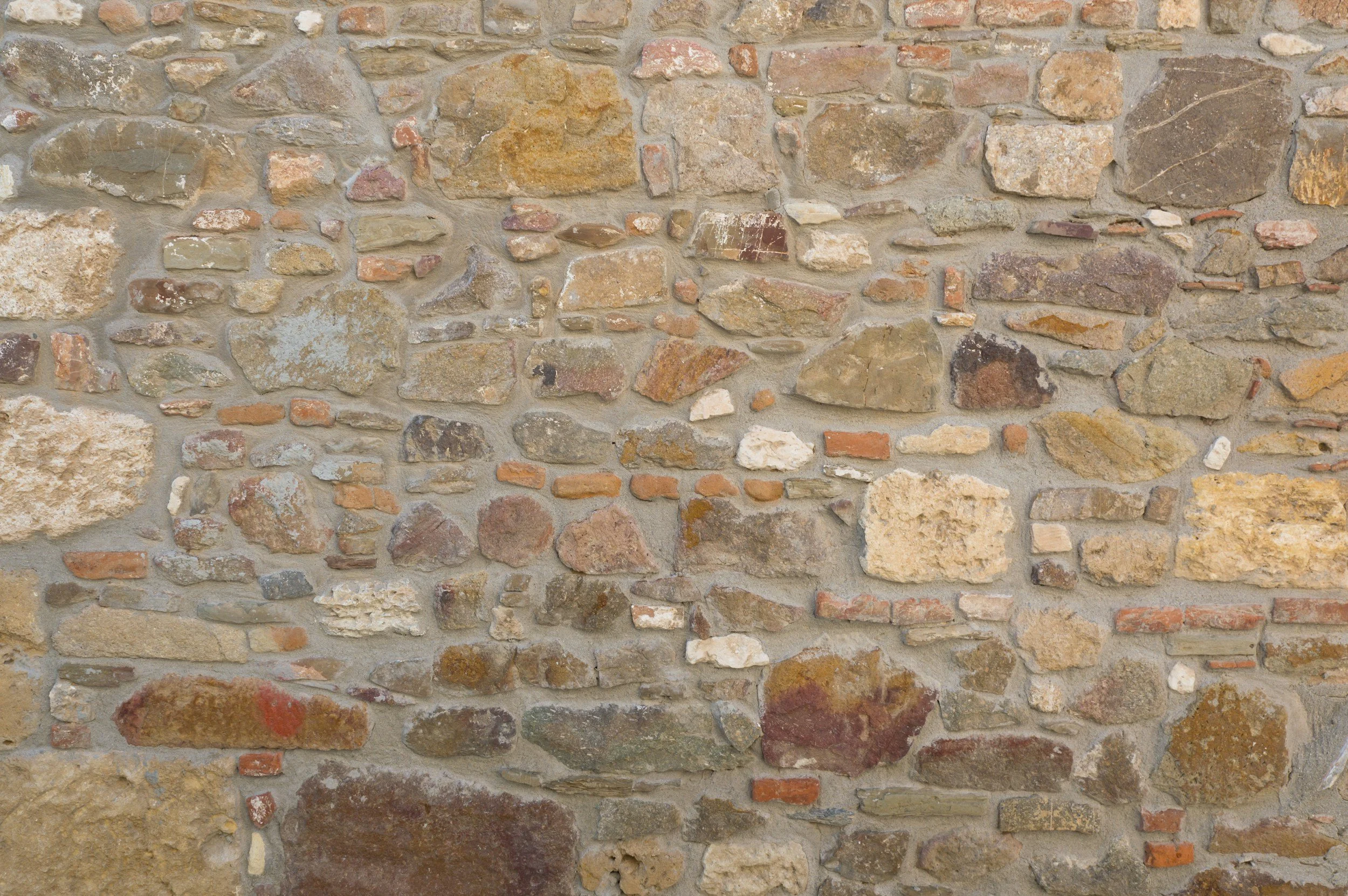 A close-up view of an old stone brick wall with varied rough-textured stones and reddish-brown bricks, held together with mortar.