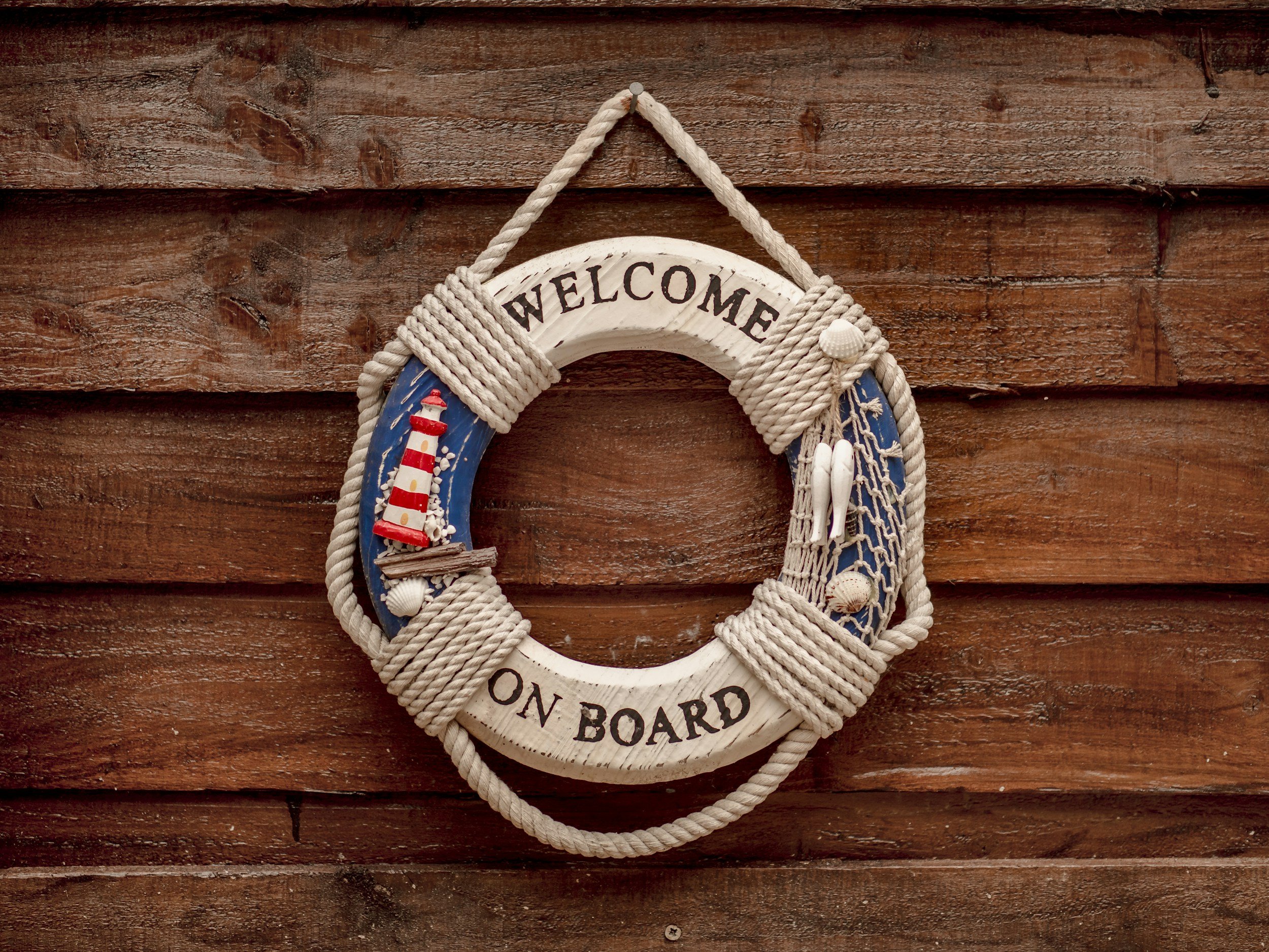 Image of a wooden sea themed life ring, an ornament saying welcome on board, a symbol of businesses onboarding clients and welcoming them.