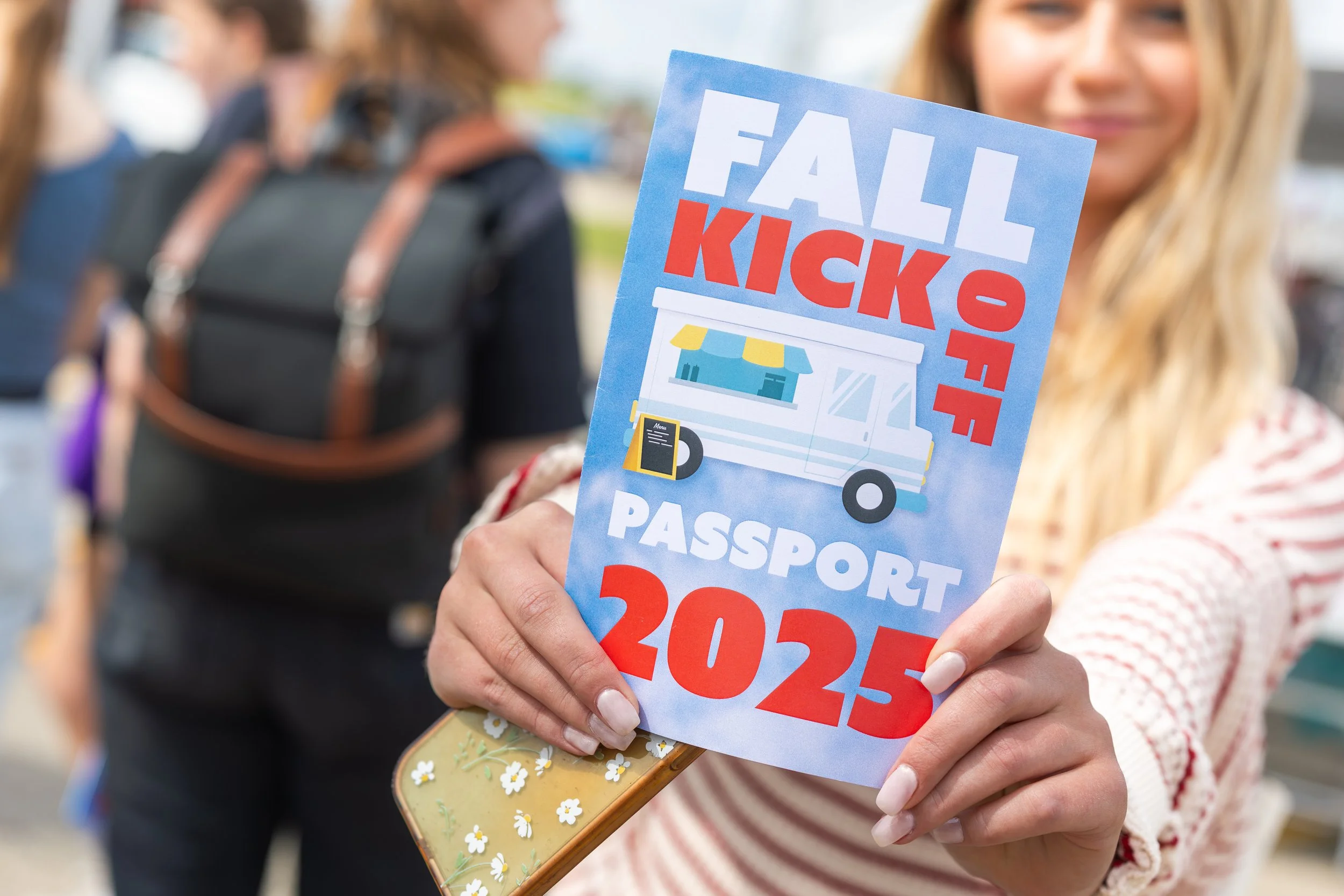 female student holding a small flyer that reads Fall Kick Off Passport 2025 with an illustration of a food truck on the front of it