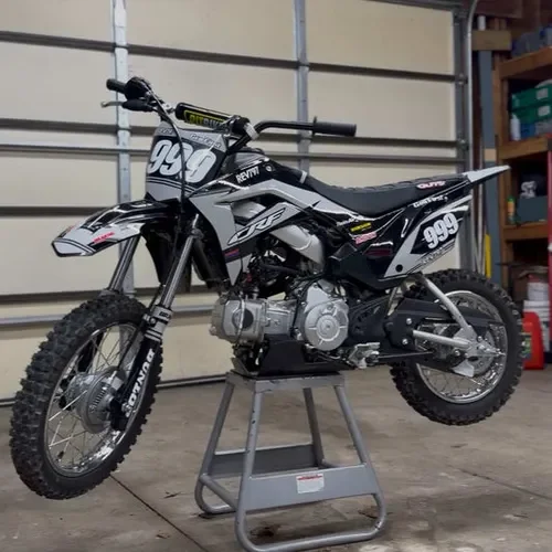 Black and white dirt bike on stand inside a garage with shelves and tools.