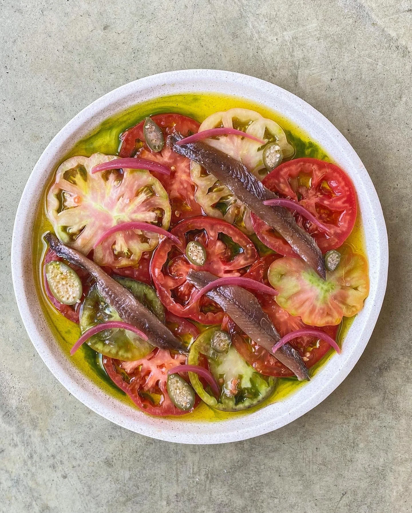 Plated dish of heirloom tomatoes, Olosagasti anchovies, caperberries and pickled red onions from a Studio Cibo private dining experience